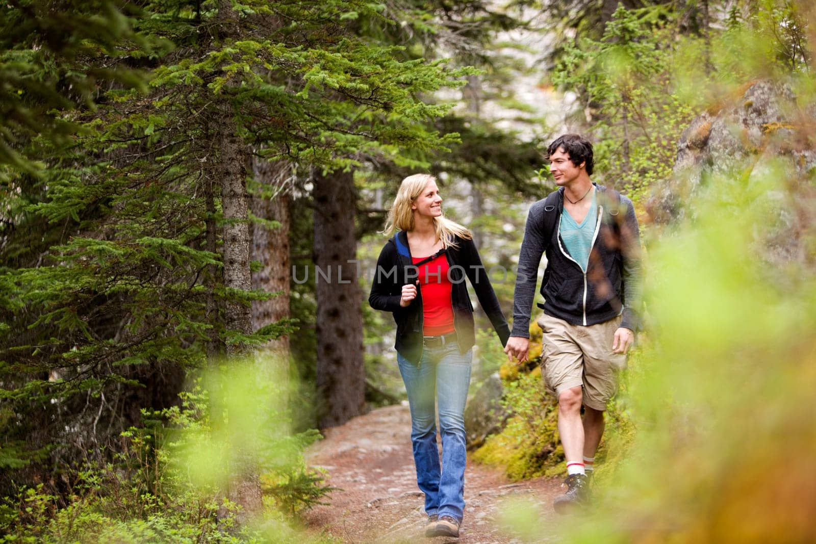A happy couple looking at eachother and walking in the forest holding hands