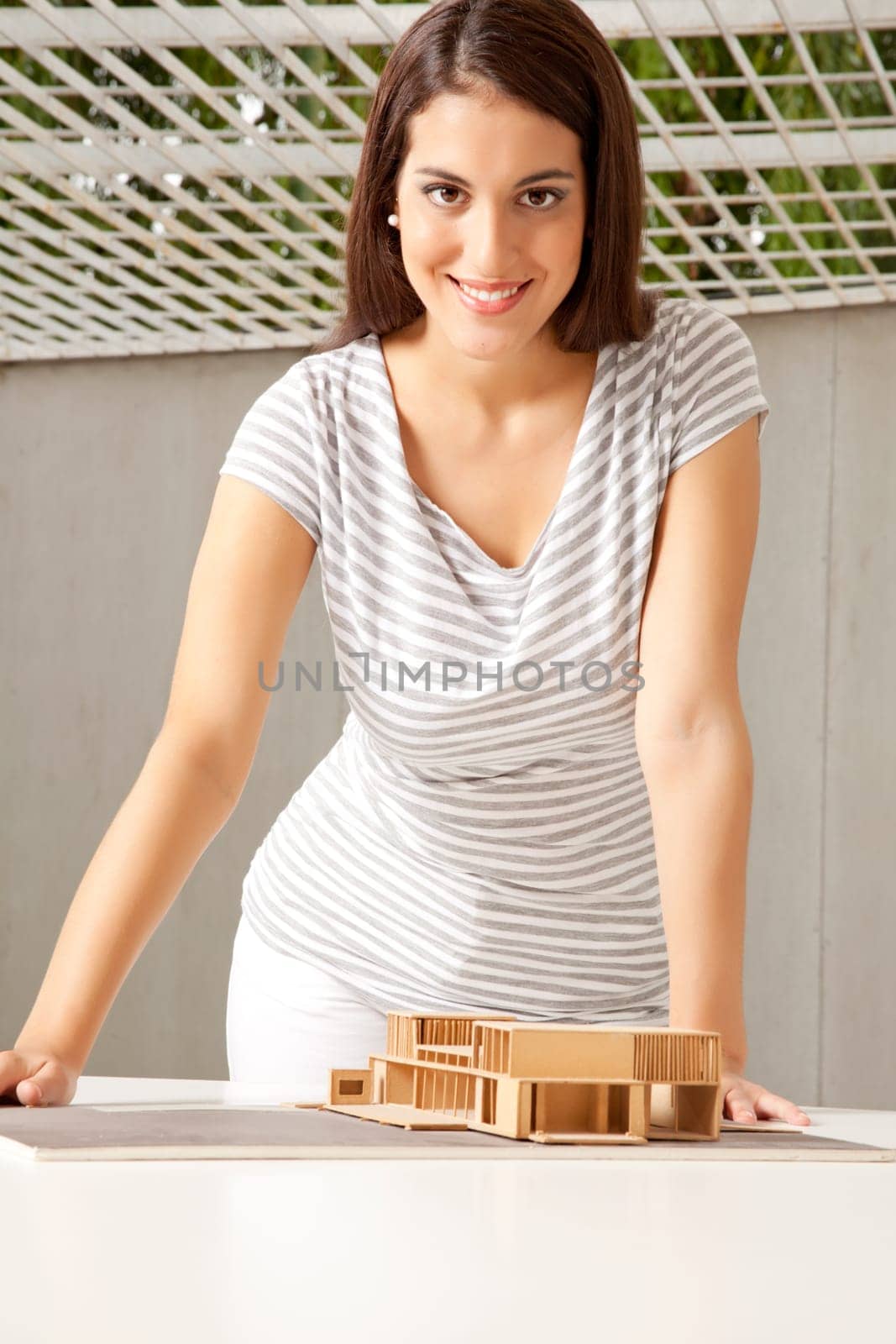 A young female architect looking at the camera with a house model on the desk