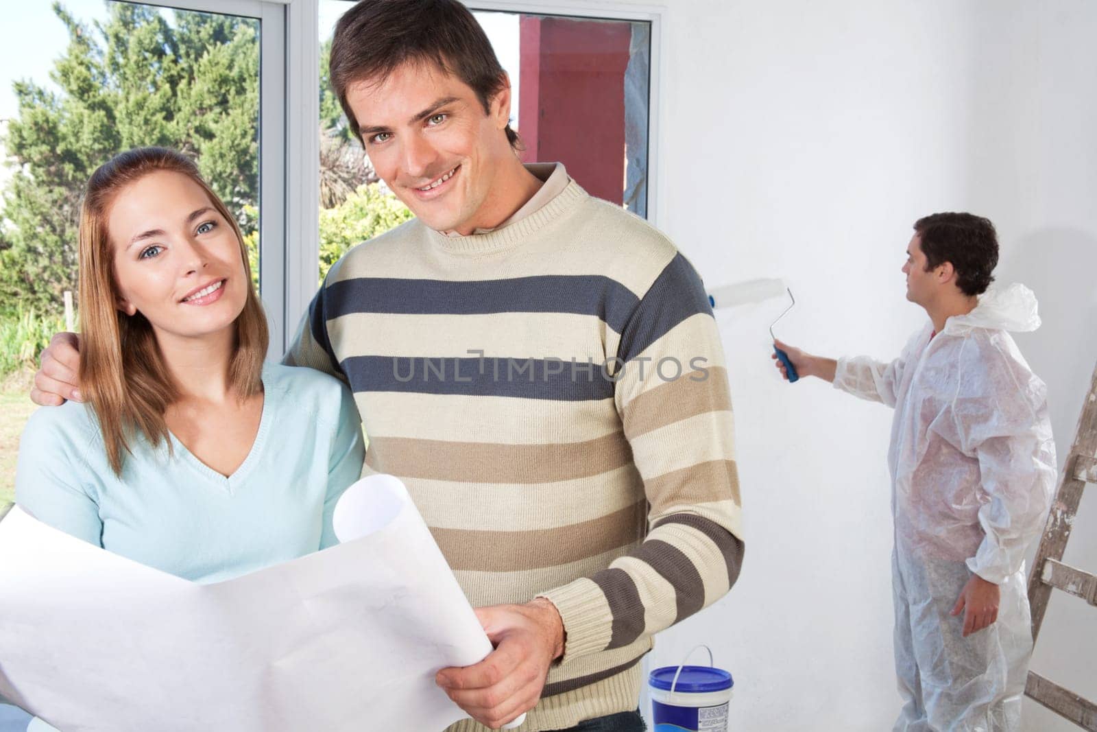 Portrait of happy couple together while painter painting the wall
