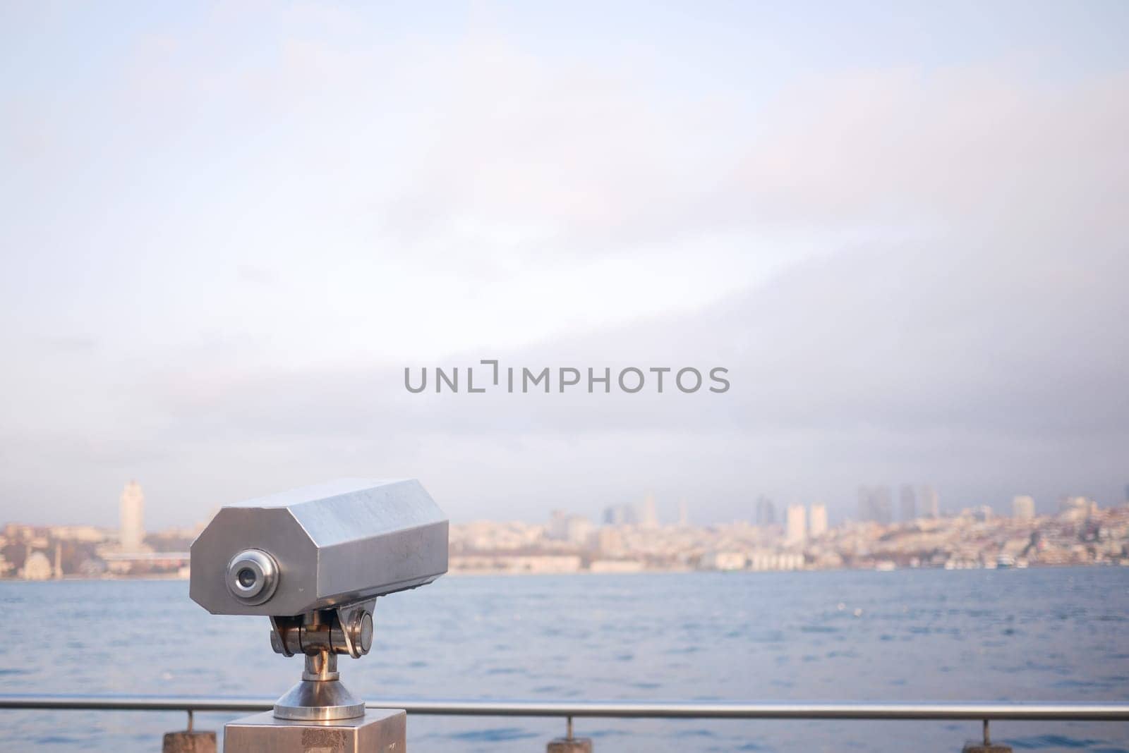 A viewfinder stands on a waterfront, offering a distant city view at dawn.