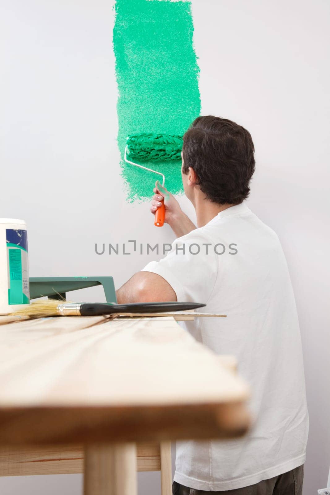 Rear view of man painting his house with color roller