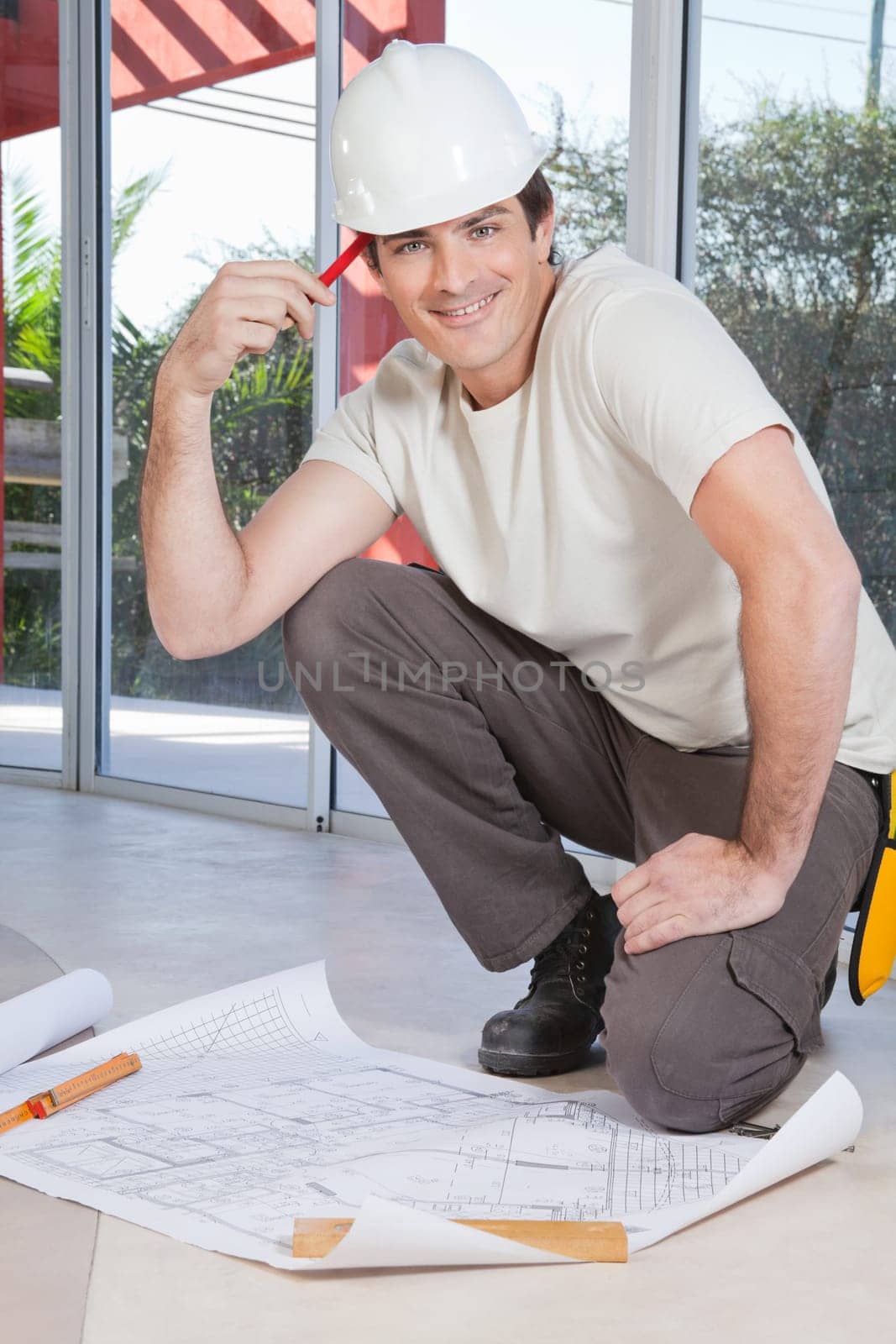 Smart young construction worker smiling with blueprint on floor