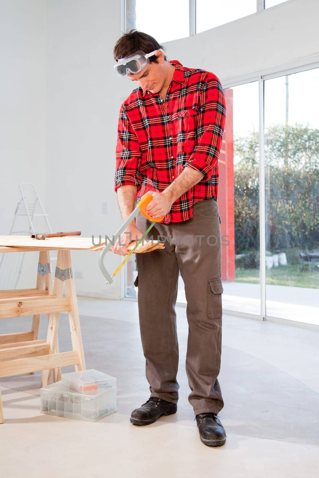A carpenter cutting wood with a hand saw in a house