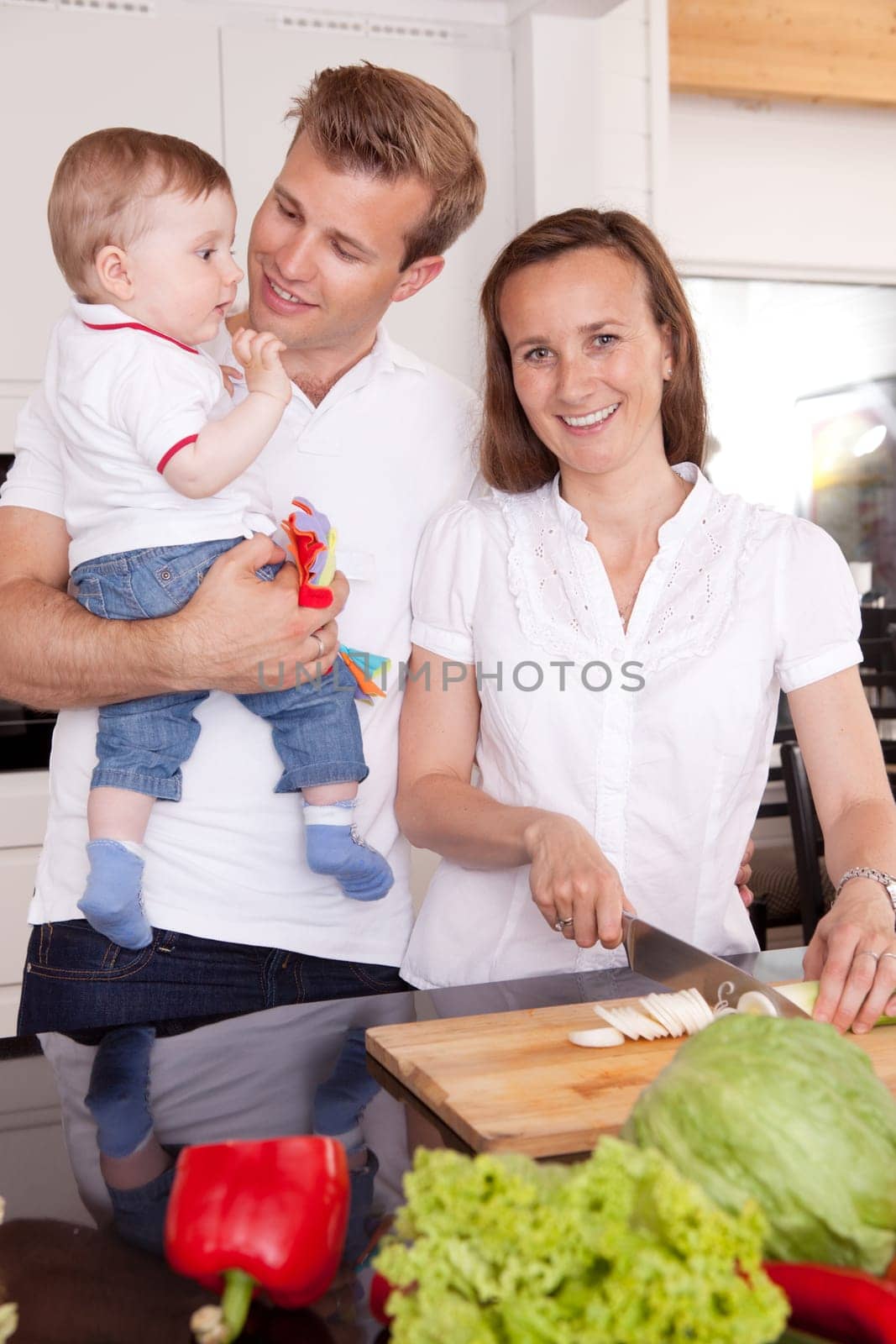 Happy young family with mother father and young toddler son in the kitchen preparing food