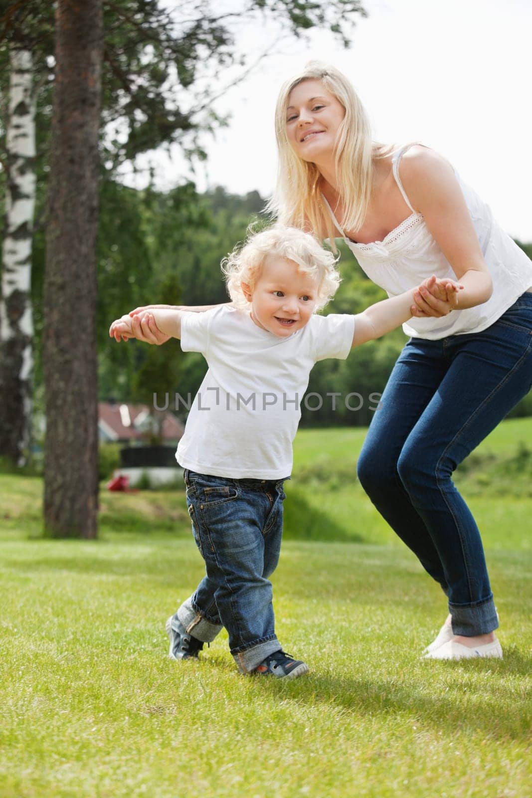 Beautiful young mother helping her adorable little boy to walk