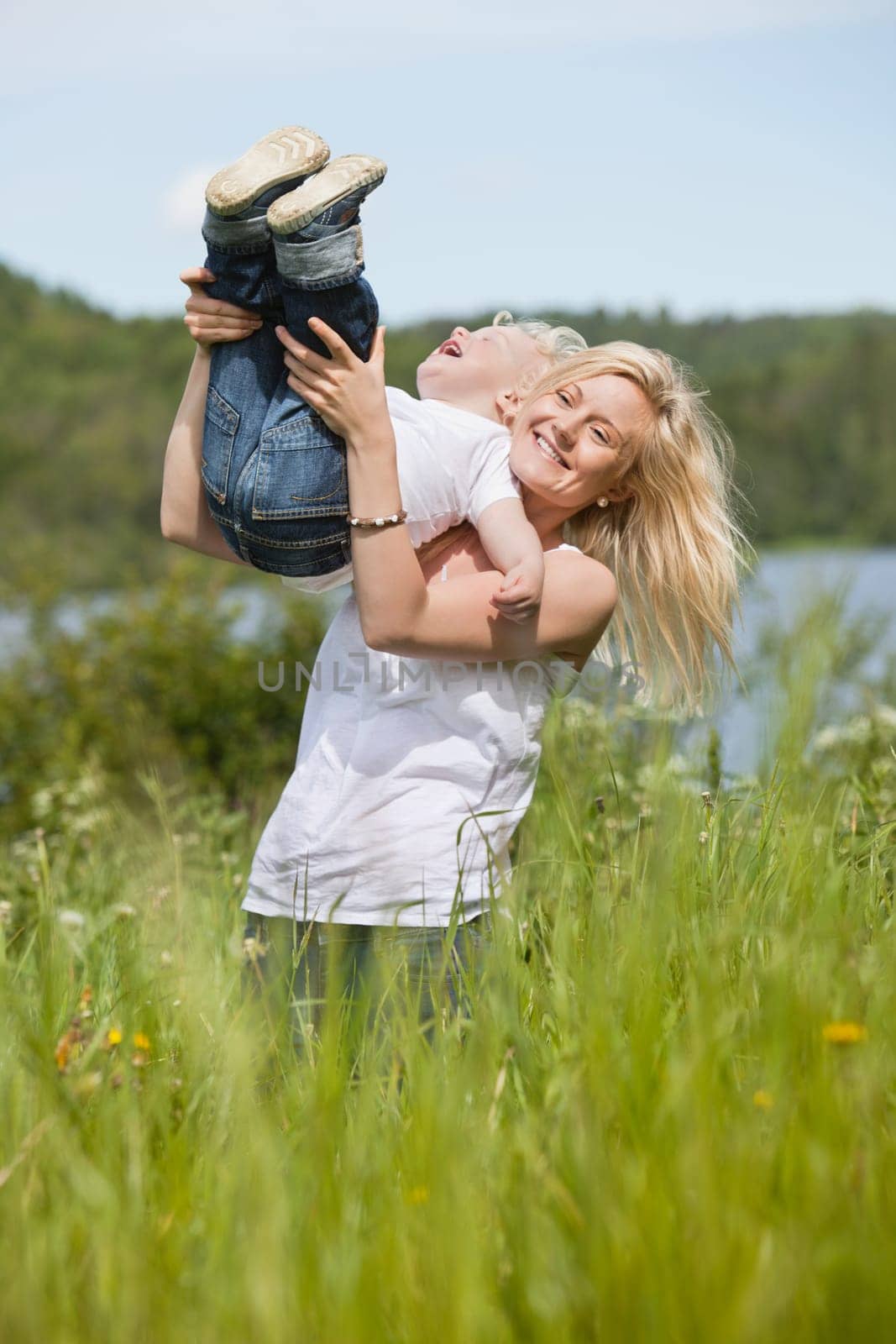 Blond woman standing in meadow playing with toddler son