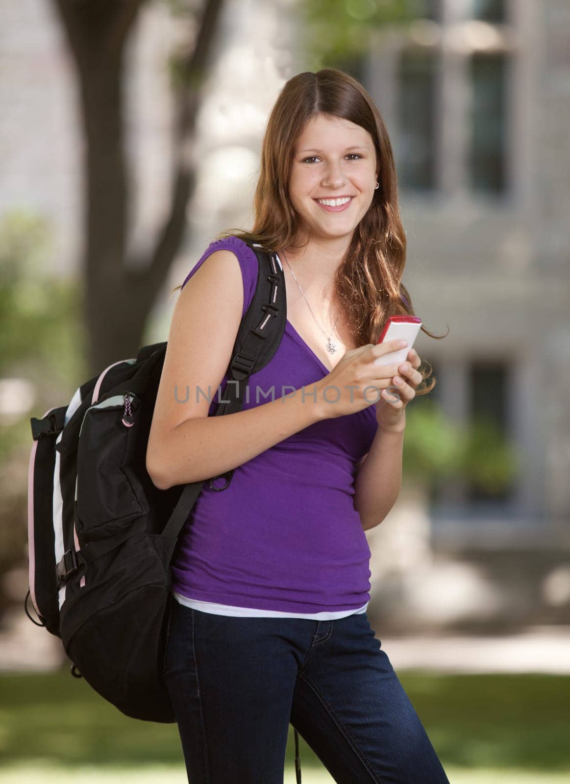 Happy young university student holding cell phone