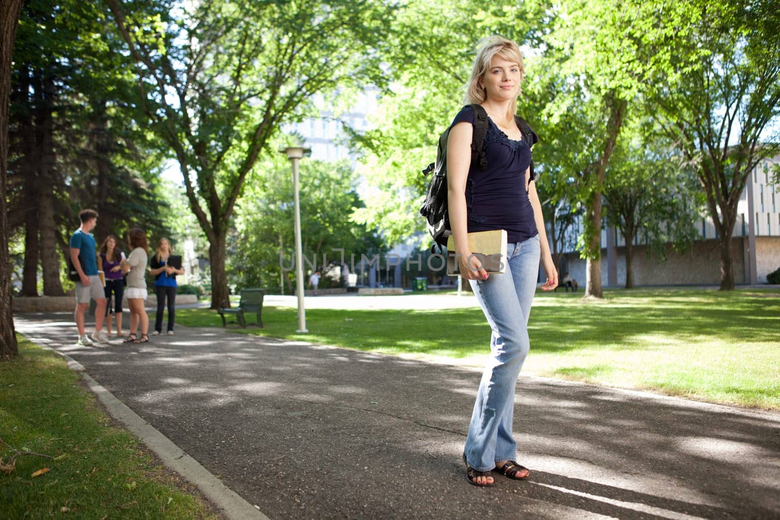 Young blond college girl walking to class with friends in background