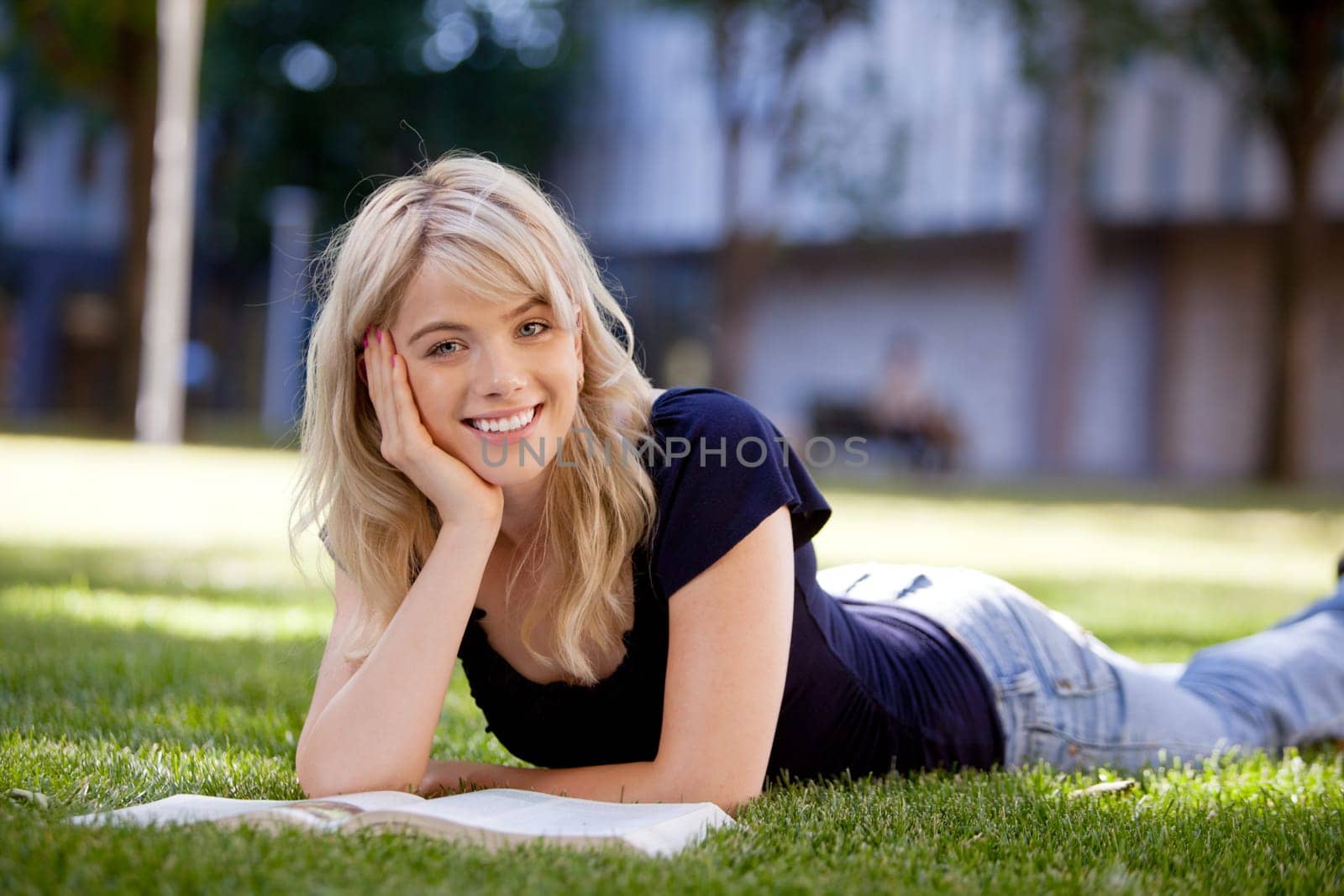 Portrait of an attractive university student studying while laying outdoors on grass