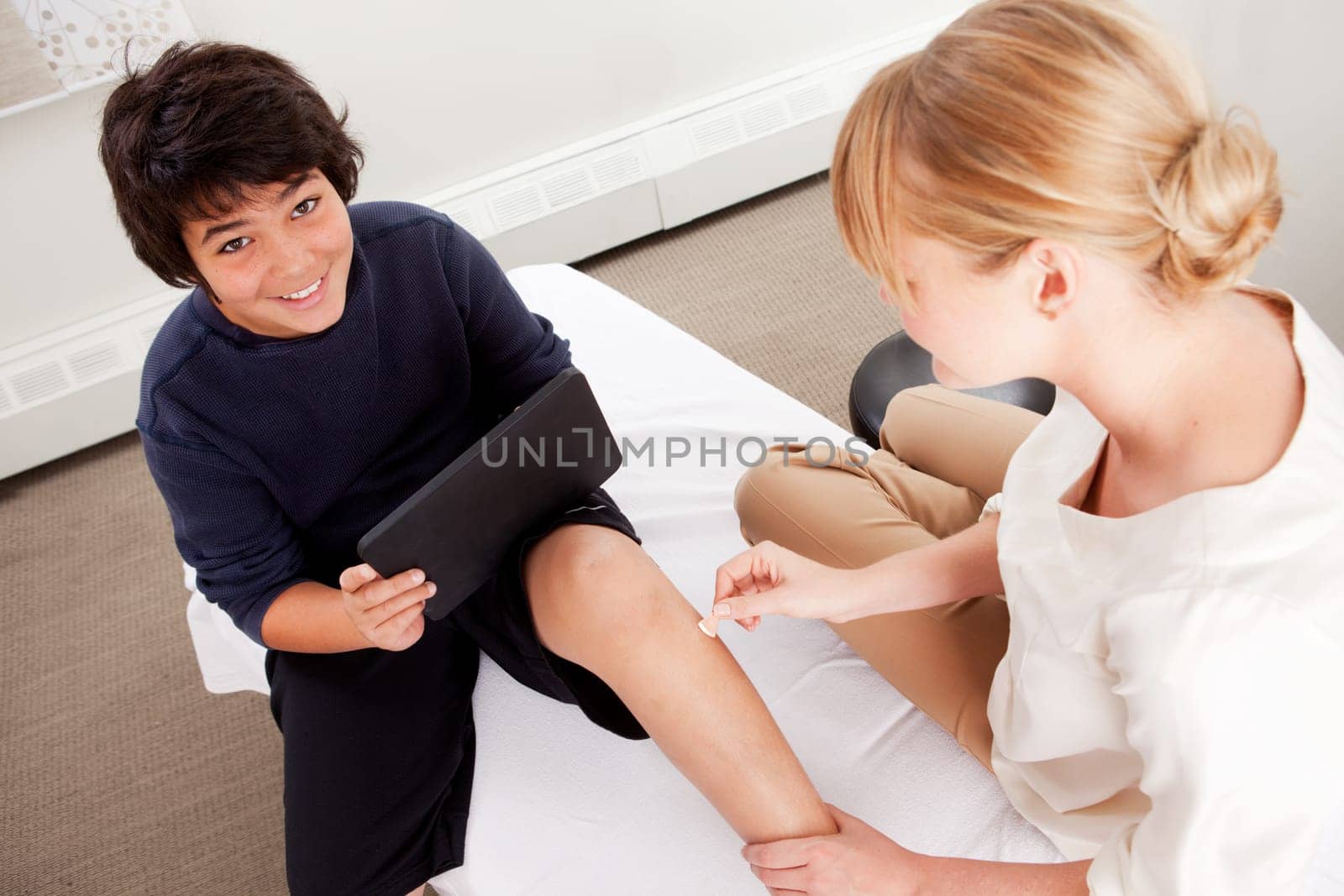 Young male receiving pediatric acupuncture while playing games on a digital tablet