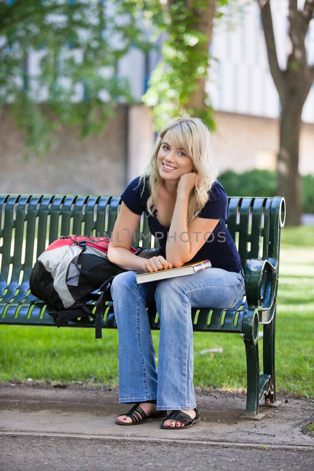 Portrait of young smiling female student sitting on bench at college campus