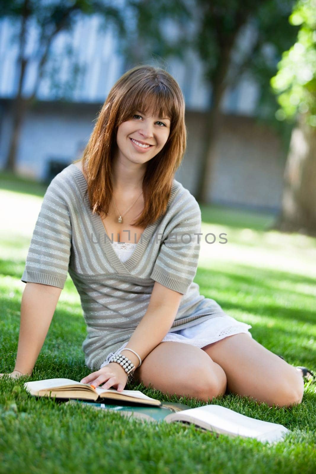 Young college student sitting with a book on campus lawn