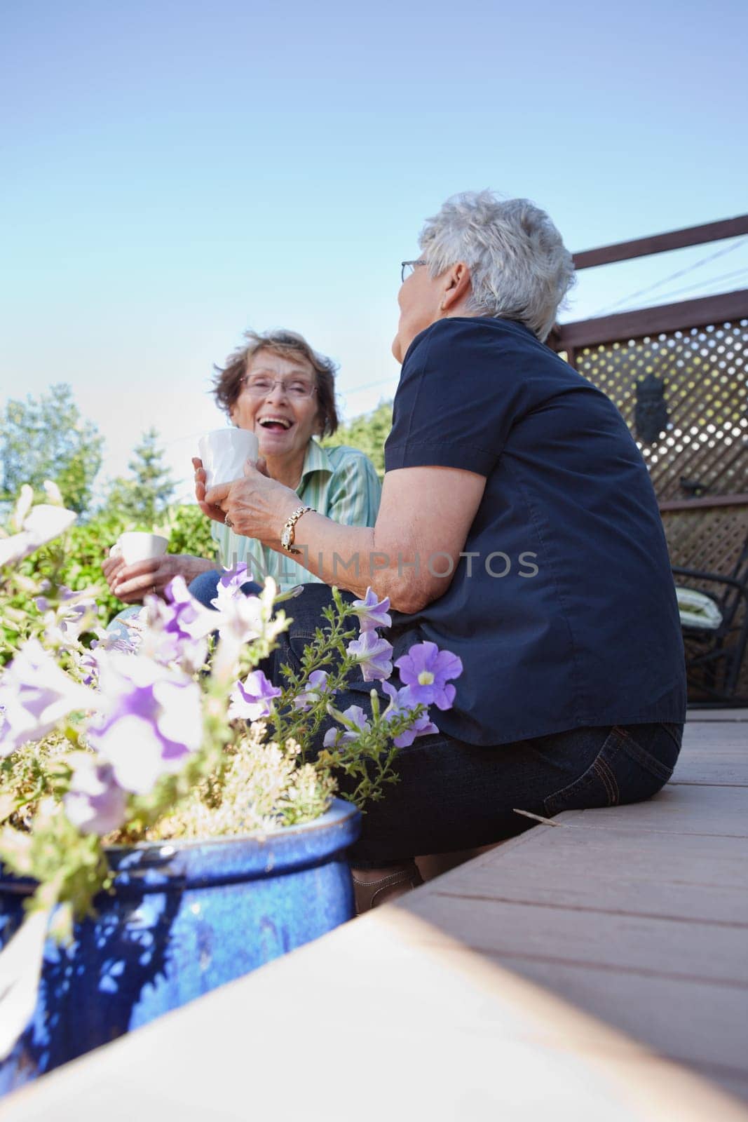Two senior women in back yard drinking warm drinks and laughing together