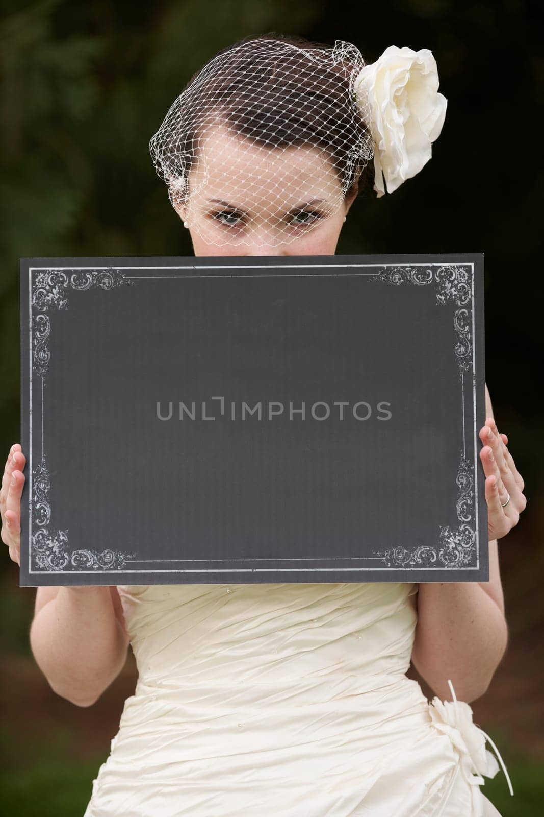 Pretty bride in wedding dress holding a blank board in front of face with space for copy