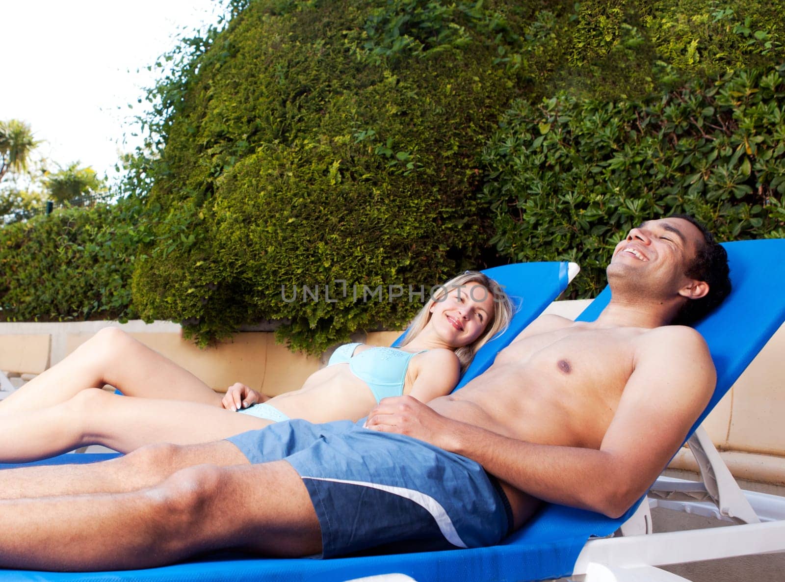 A couple suntanning on beach chairs beside a pool