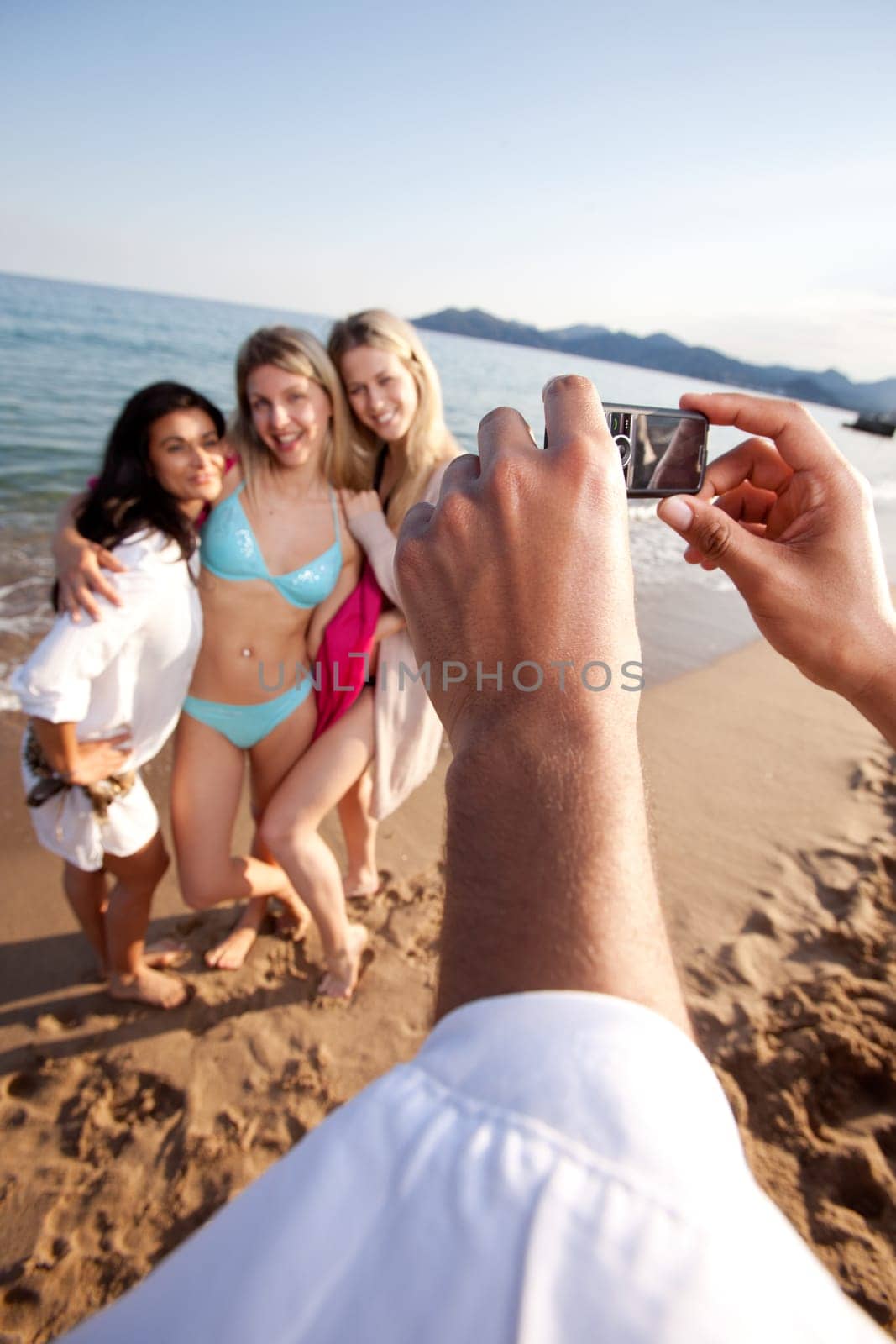 A person taking a picture of three women with a camera phone.  Shallow depth of field, focus on camera
