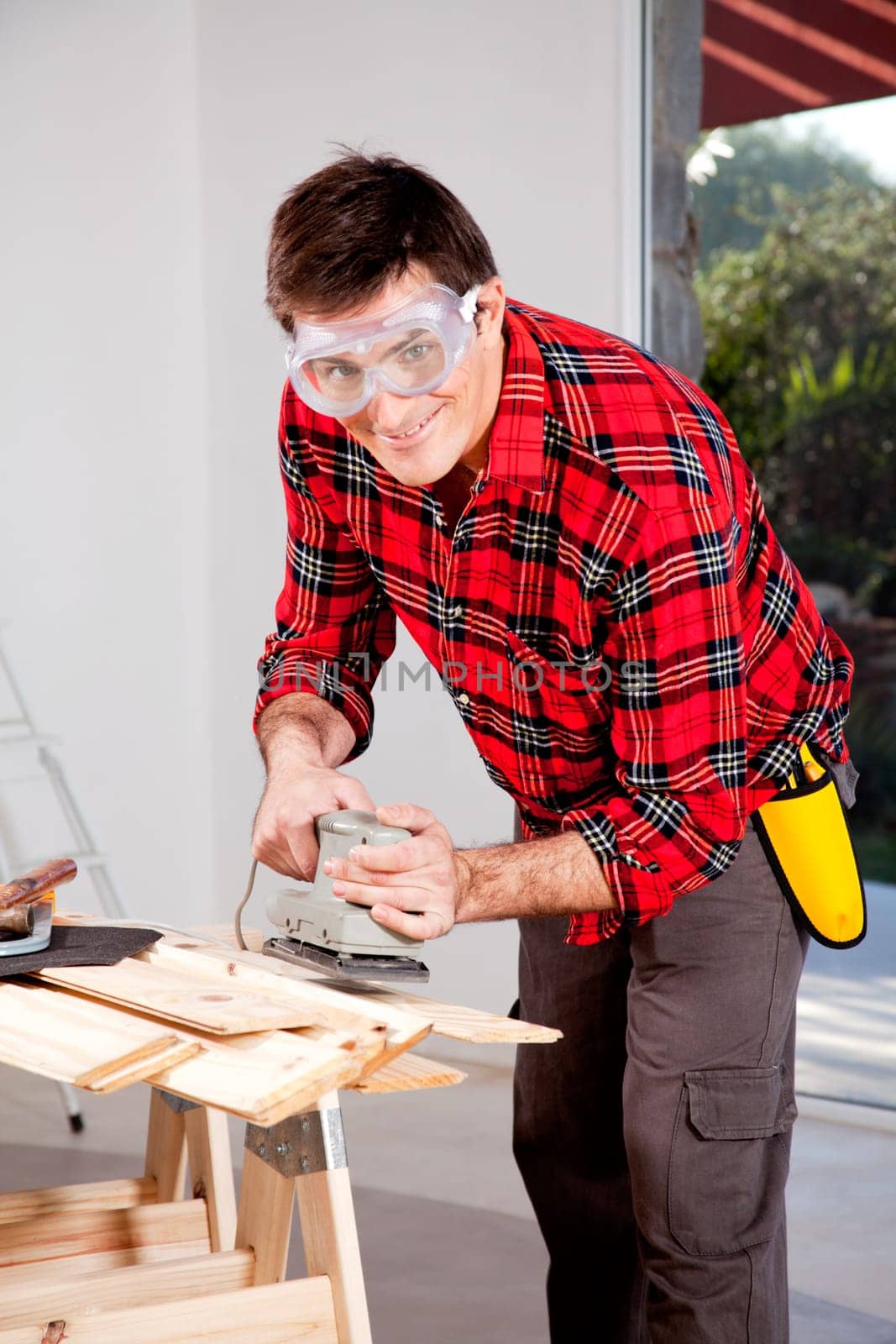 A man wearing saftey goggles using an electric hand sander