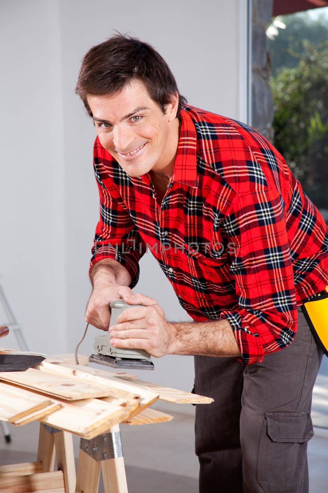 A man looking at the camera holding an electric sander