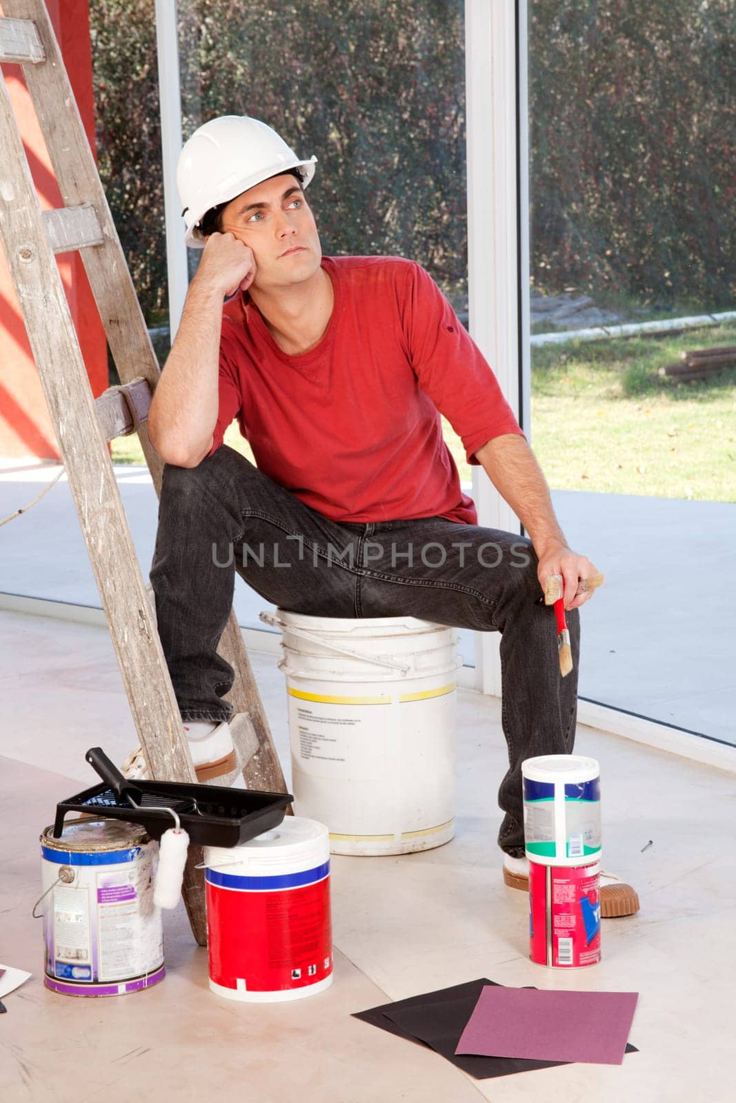 A painter sitting on a paint can, tired and resting