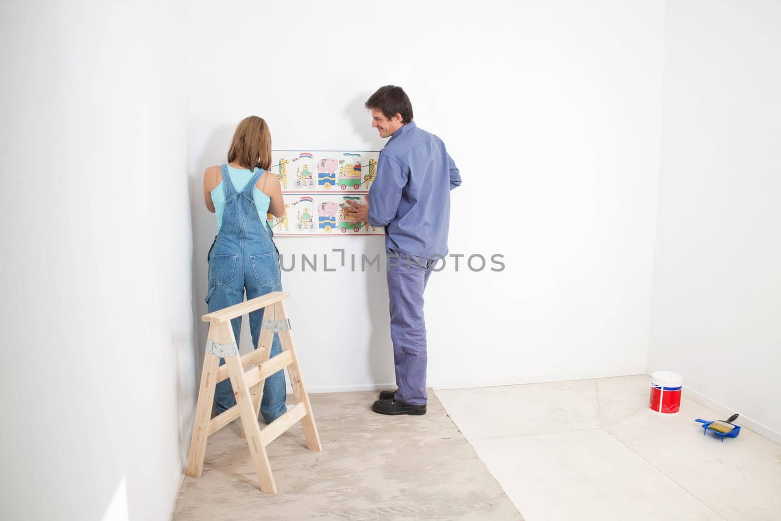 Couple putting up wall papper in baby room