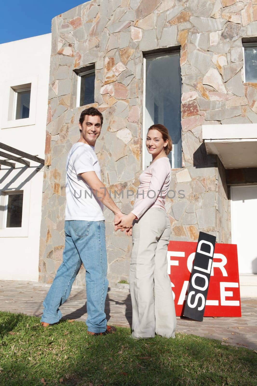 Portrait of happy couple holding hands with new house in background