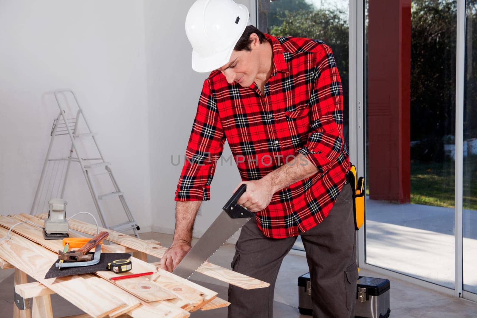 A construction worker using a hand wood saw while wearing a white safety helmet