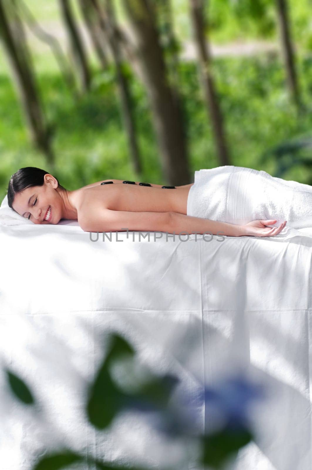 Beautiful young girl at the day spa with black stones on her bare back