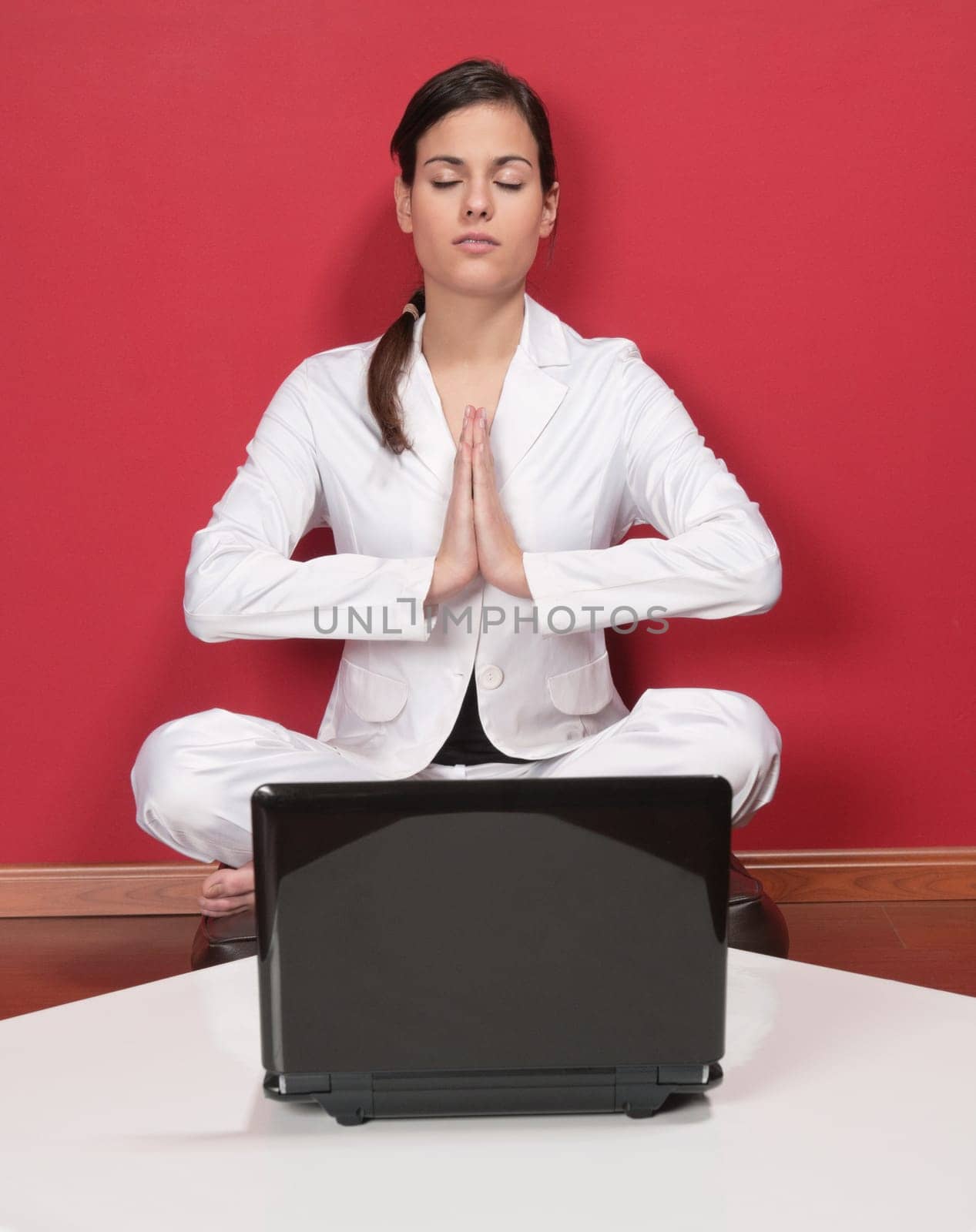 Attractive businesswoman meditating in yoga lotus position with laptop on table