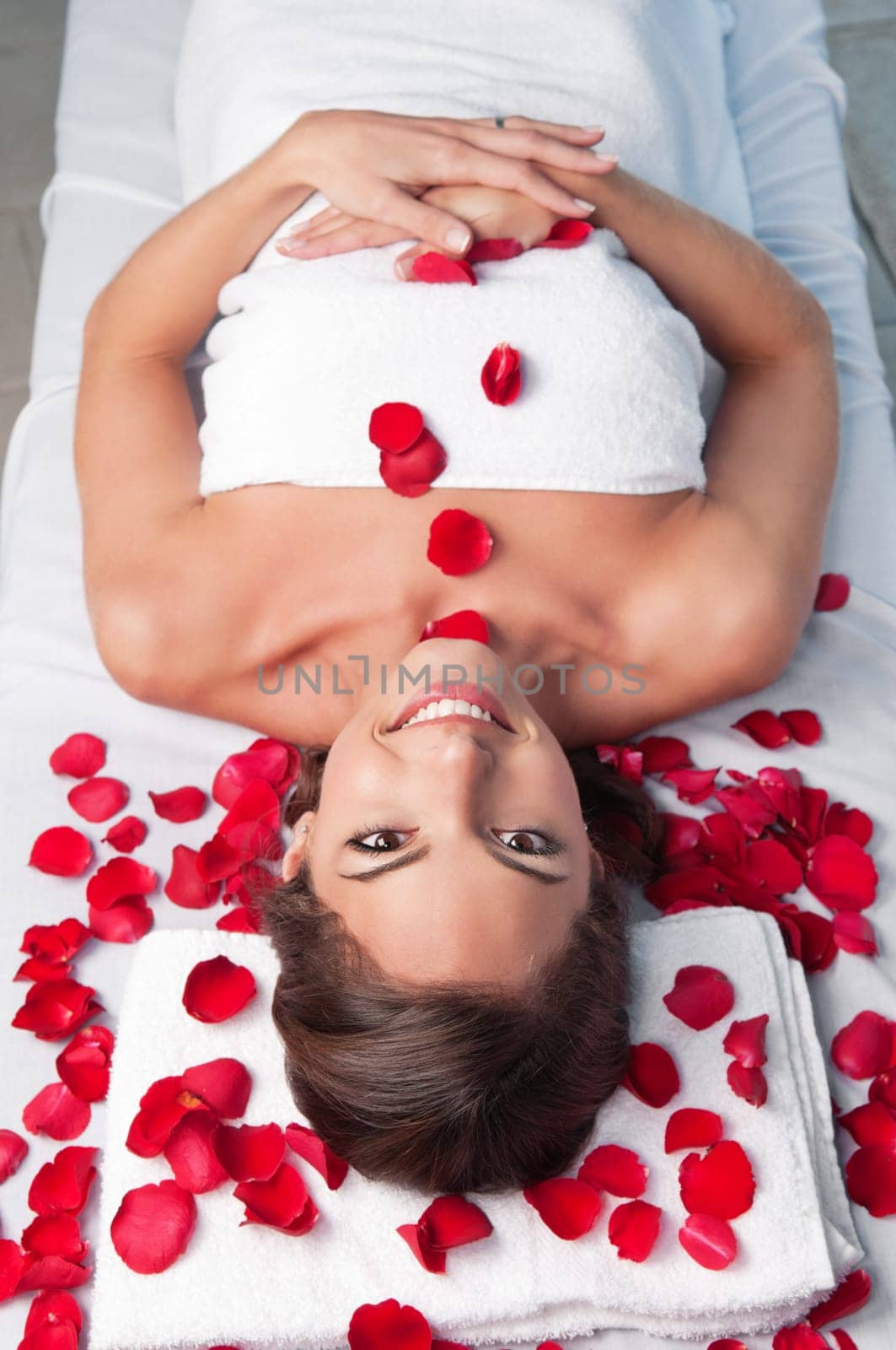 Smiling beautiful woman lying on a massage table with rose petals around