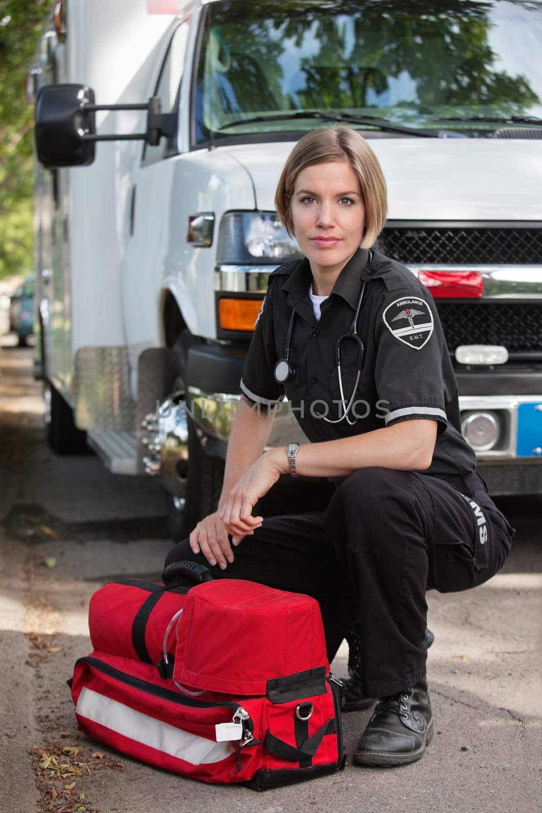 Confident EMS paramedic kneeling by portable oxygen unit and ambulance