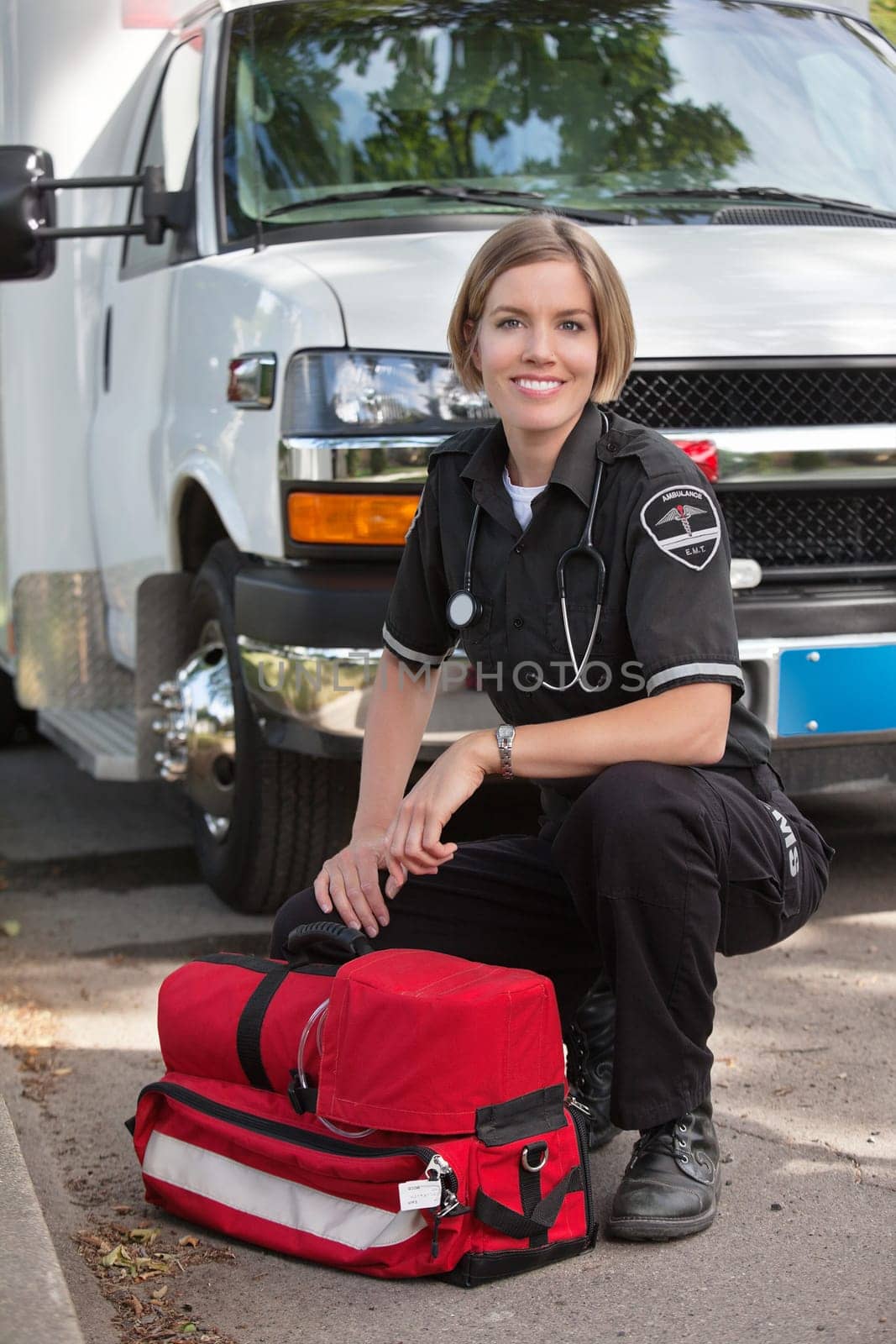 Portrait of a happy paramedic kneeling by a portable oxygen unit and ambulance