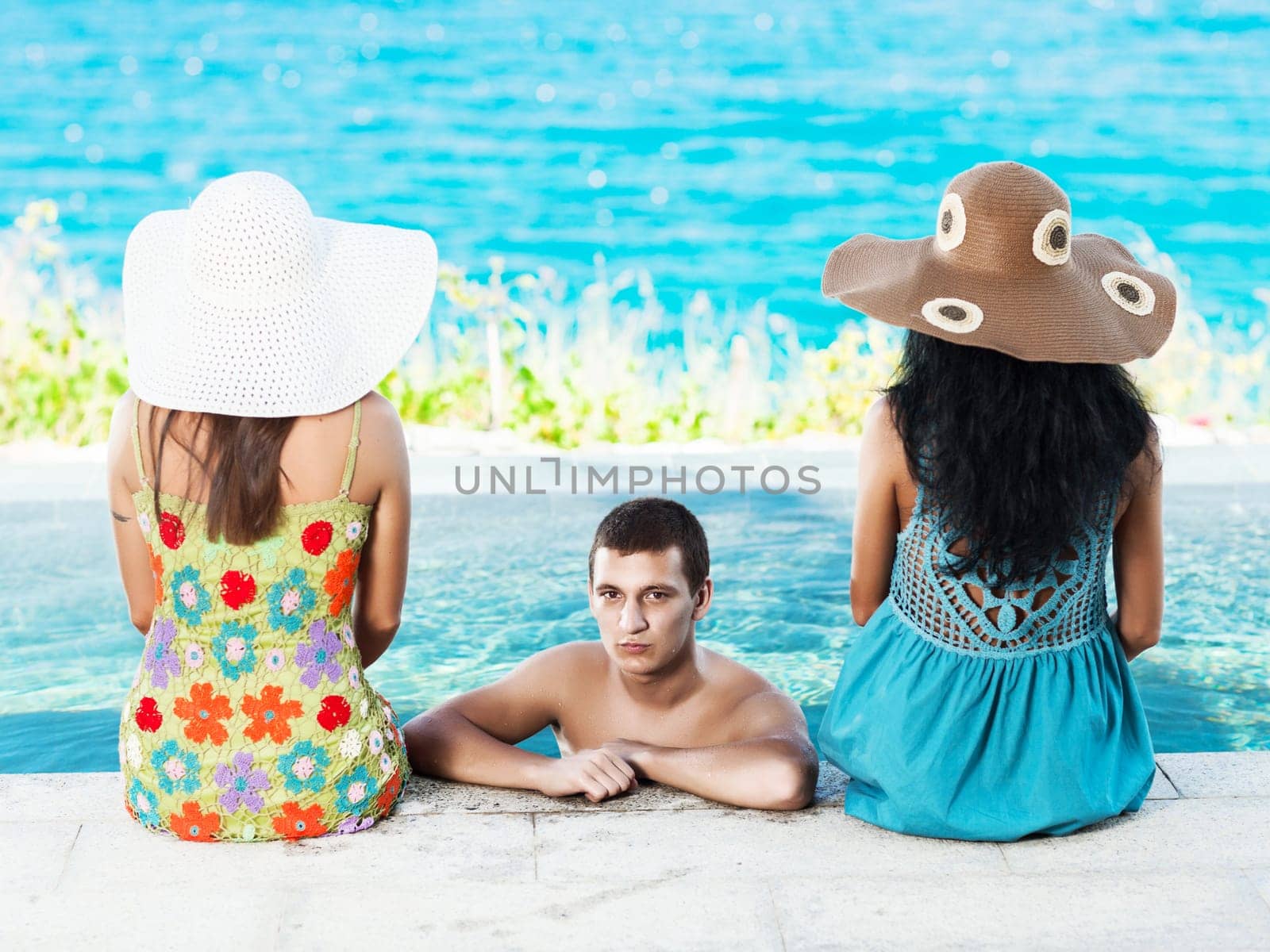 Man and two women on the edge of swimming pool