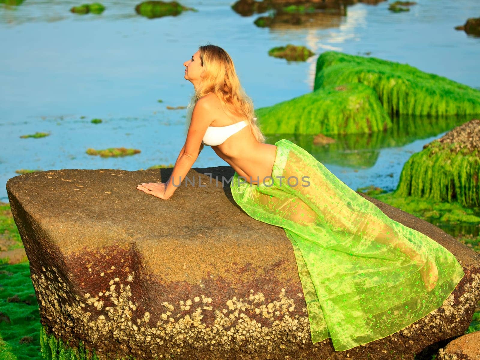 Beautiful woman like mermaid posing on the rock
