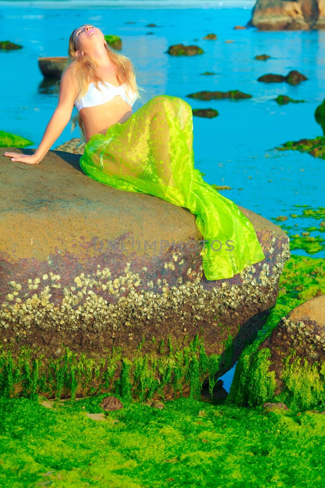 Beautiful woman like mermaid posing on the rock