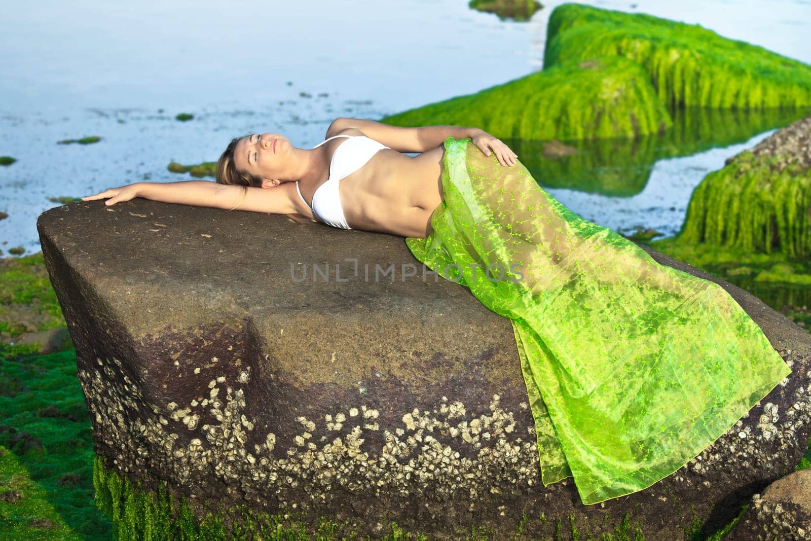 Beautiful woman like mermaid posing on the rock