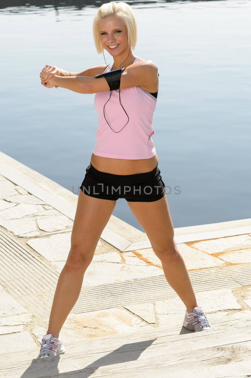Sport young woman stretch body by water pier summer day