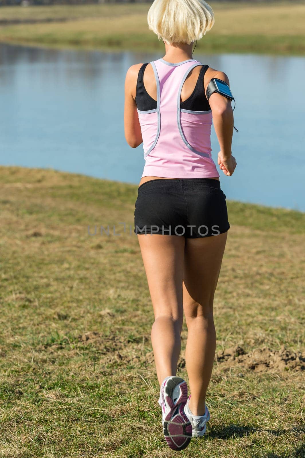Female runner jogging by water park sunny day fit body
