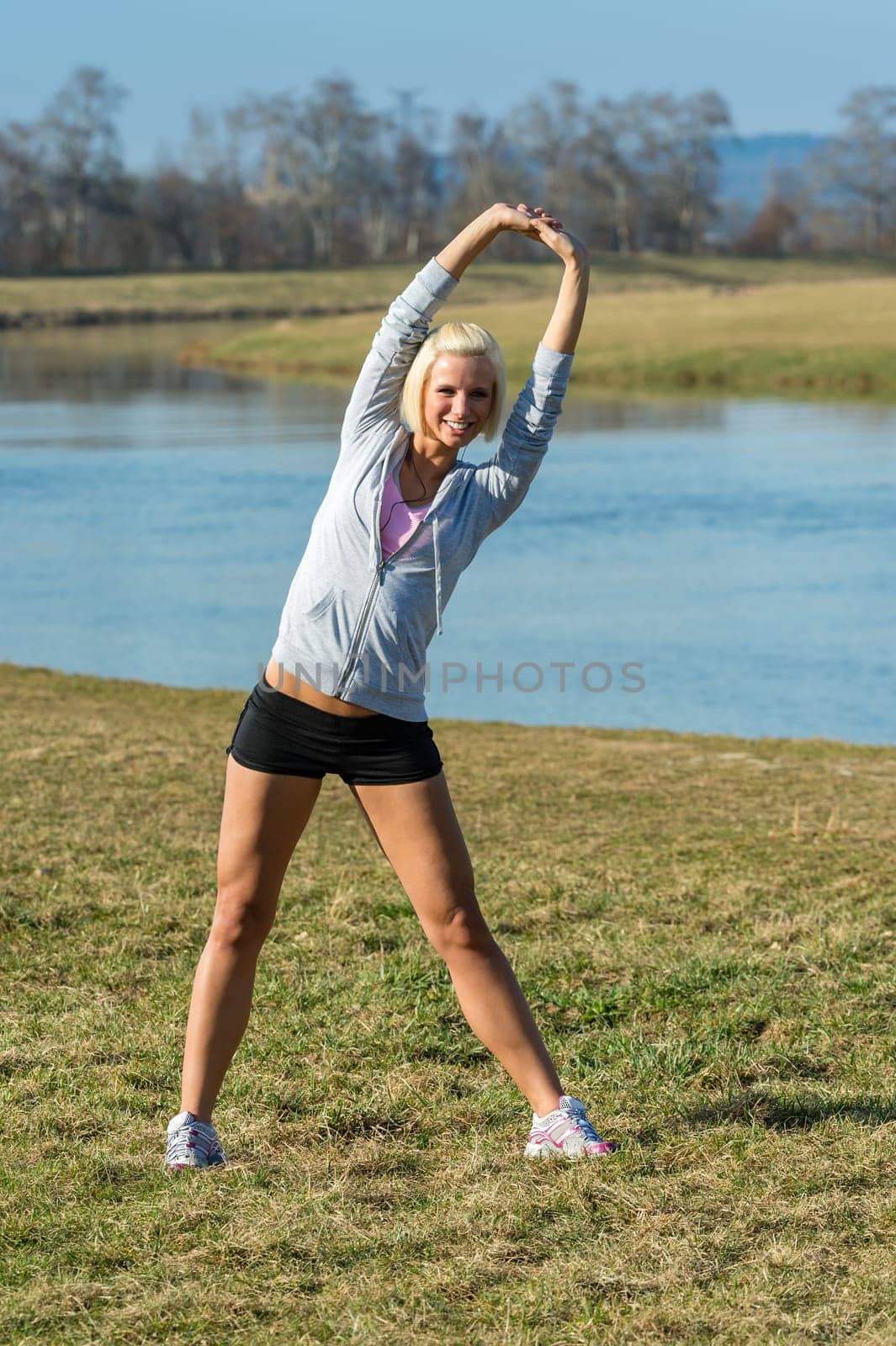 Young woman stretching outdoors before jogging workout river bank summer