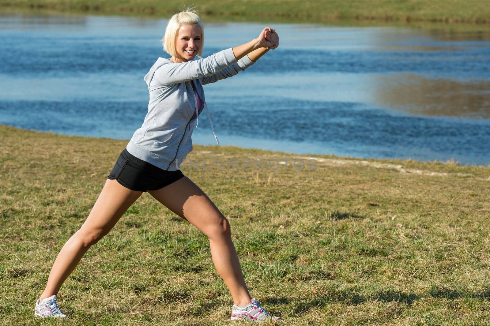 Young woman stretching outdoors before jogging workout river bank summer