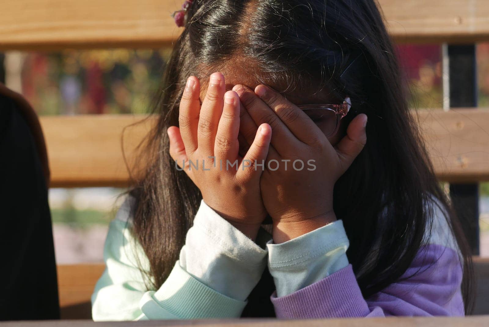 A young child hides her face with hands, expressing various emotions in a park.