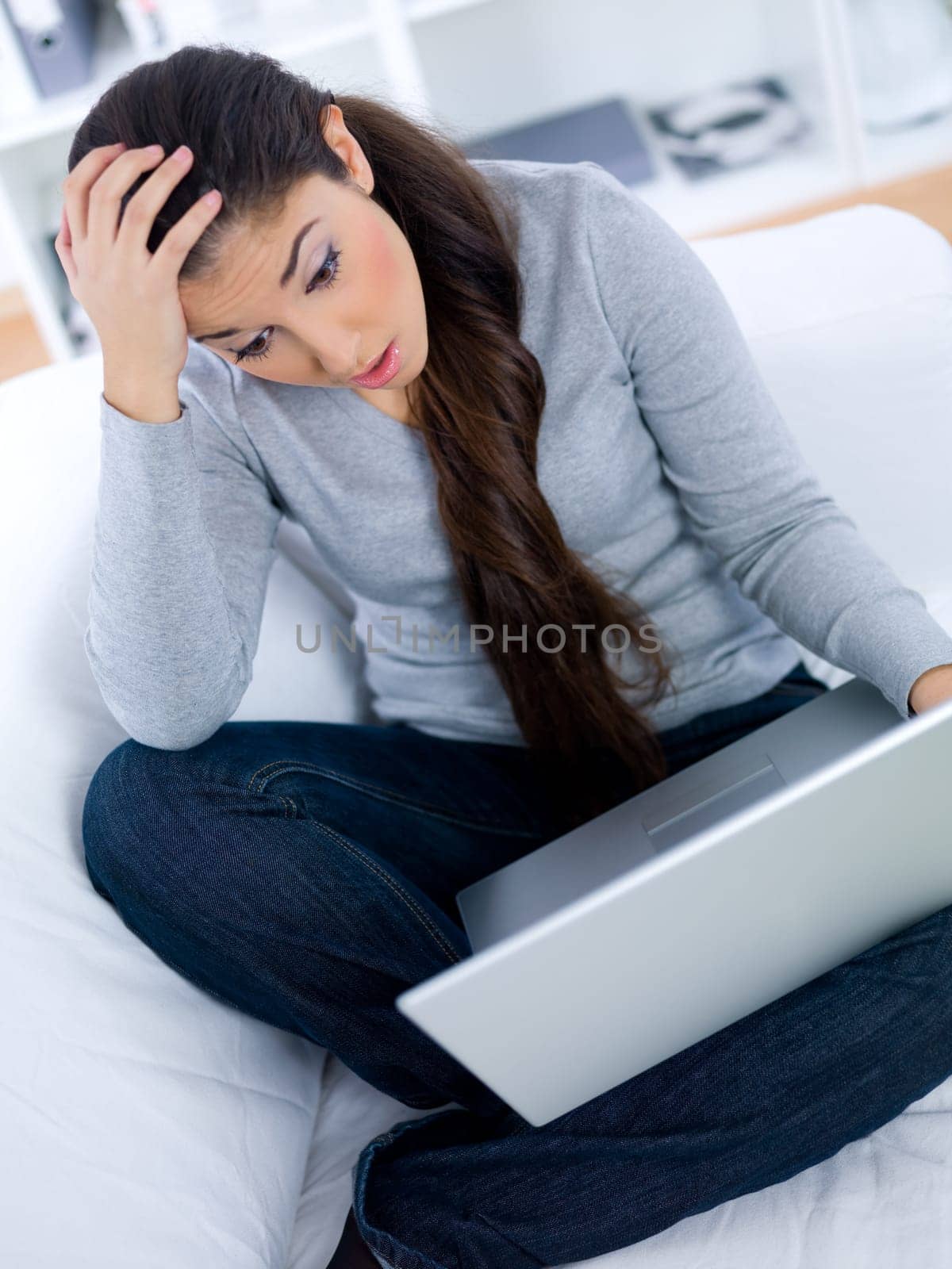 Worried young woman sitting on couch and working on laptop