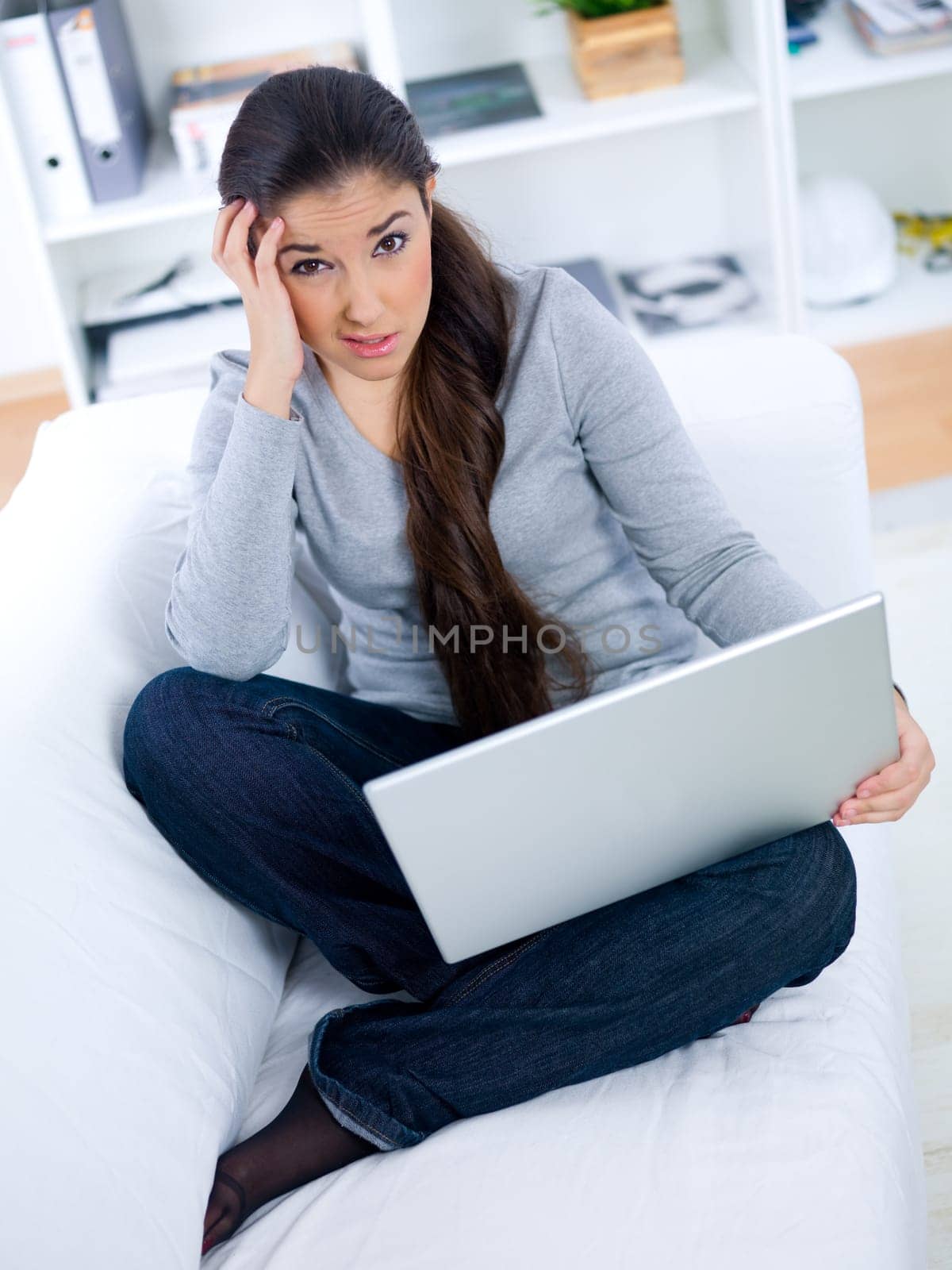 Worried young woman sitting on couch and working on laptop
