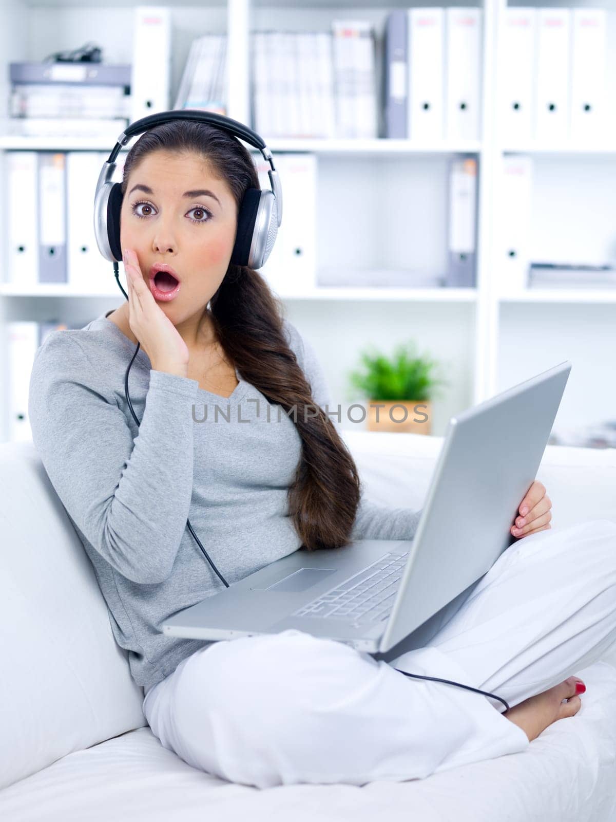 Frighted young woman sitting on couch and working on laptop