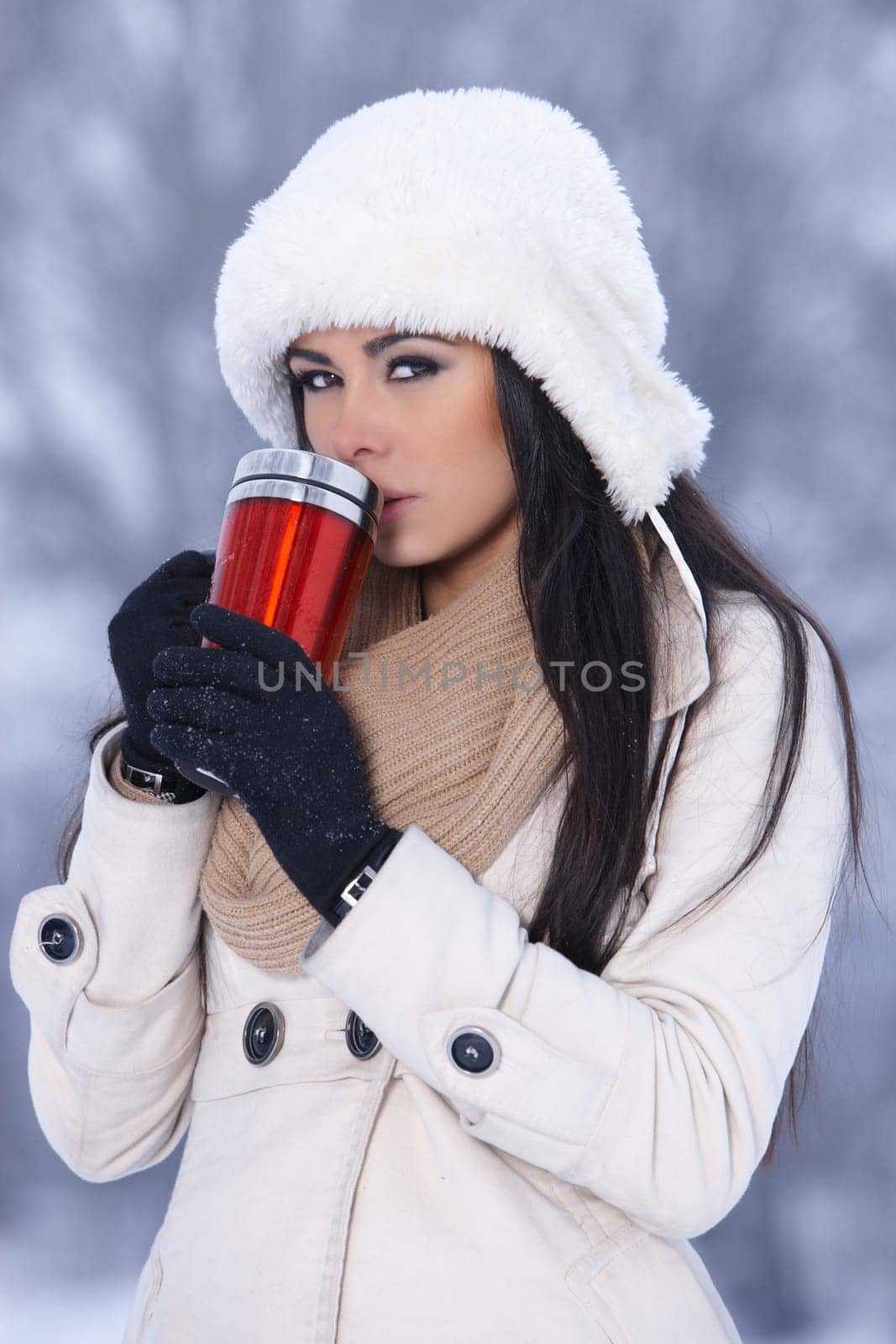 Beautiful woman holding thermal mug in snowy winter outdoors