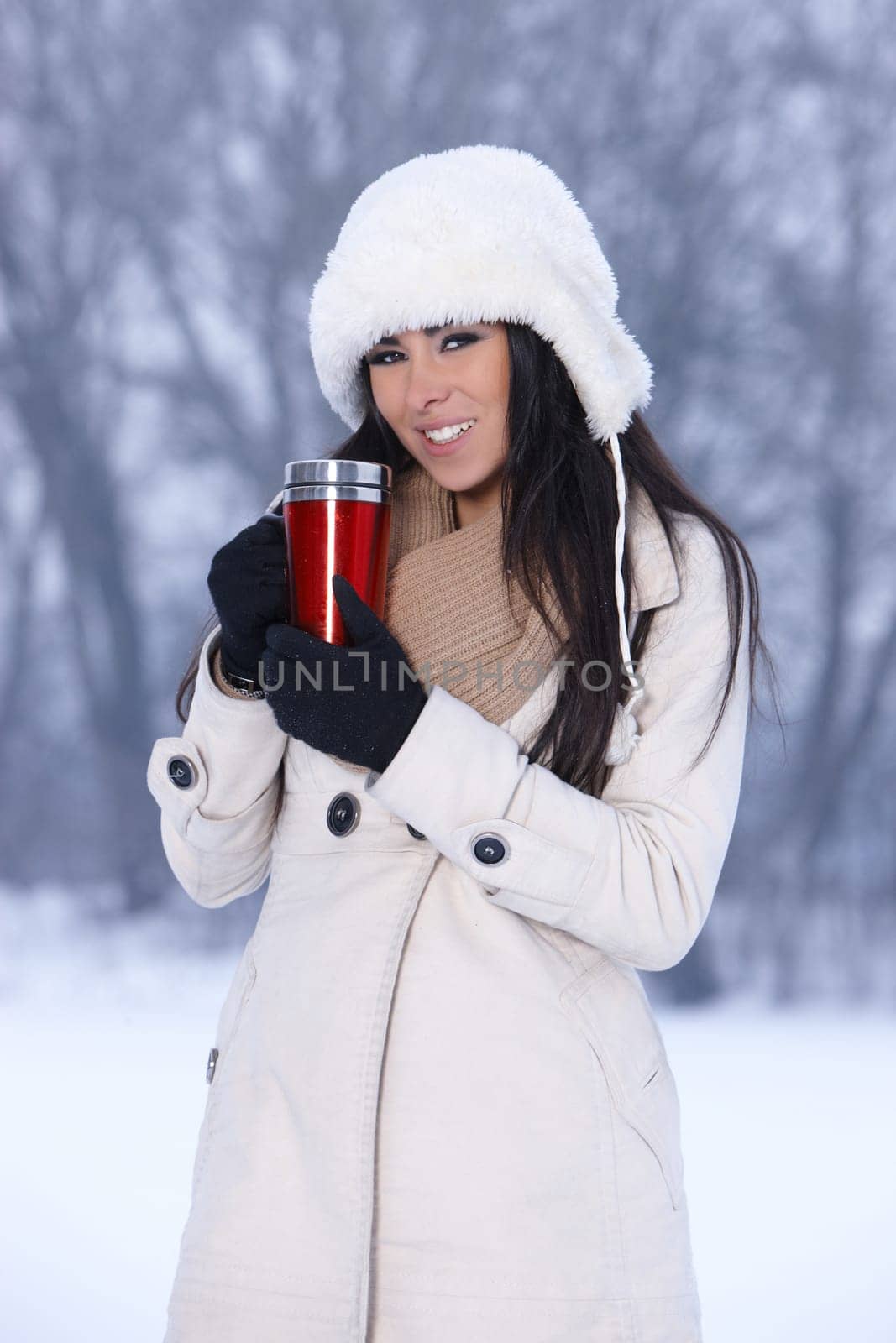 Beautiful woman holding thermal mug in snowy winter outdoors