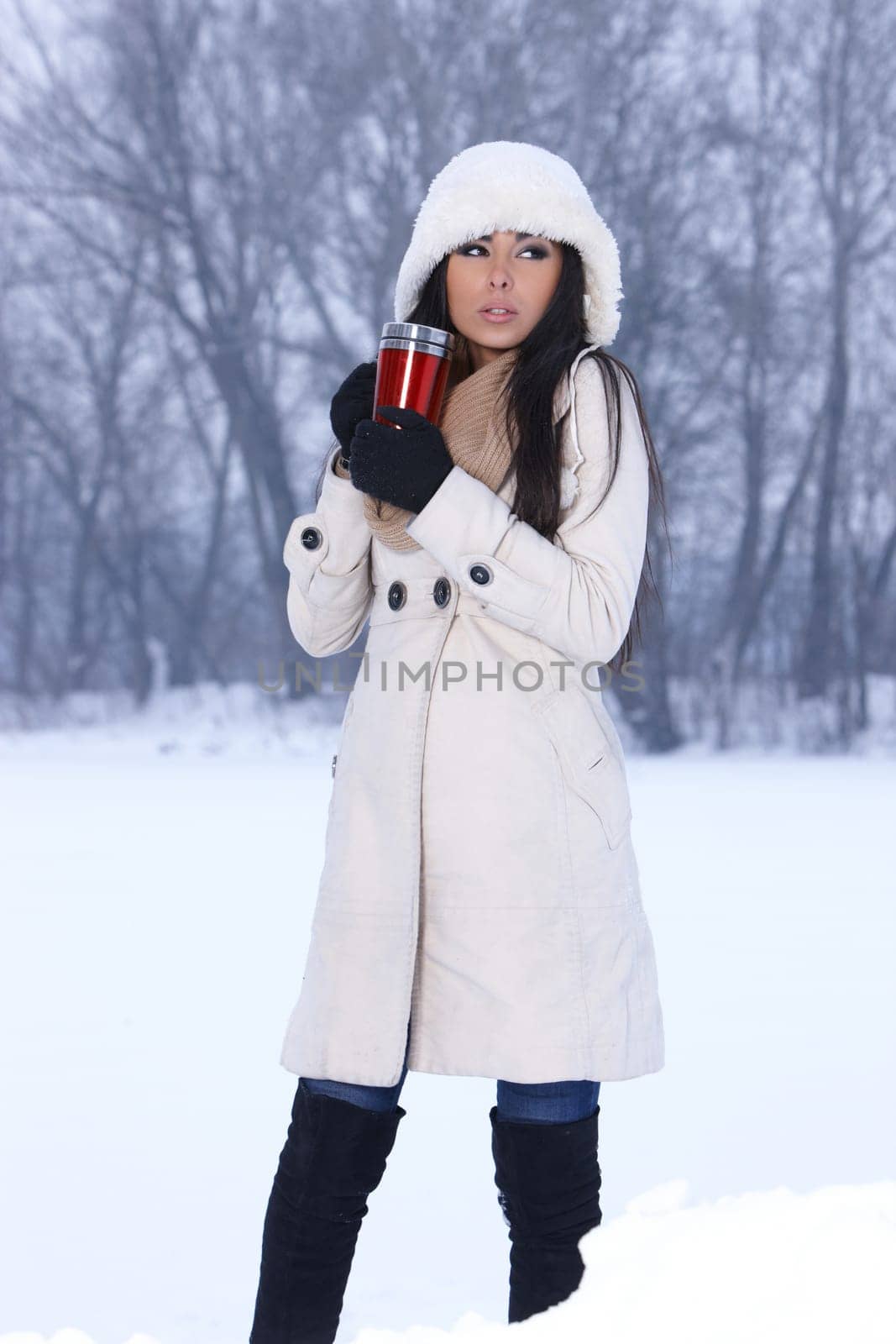 Beautiful woman holding thermal mug in snowy winter outdoors