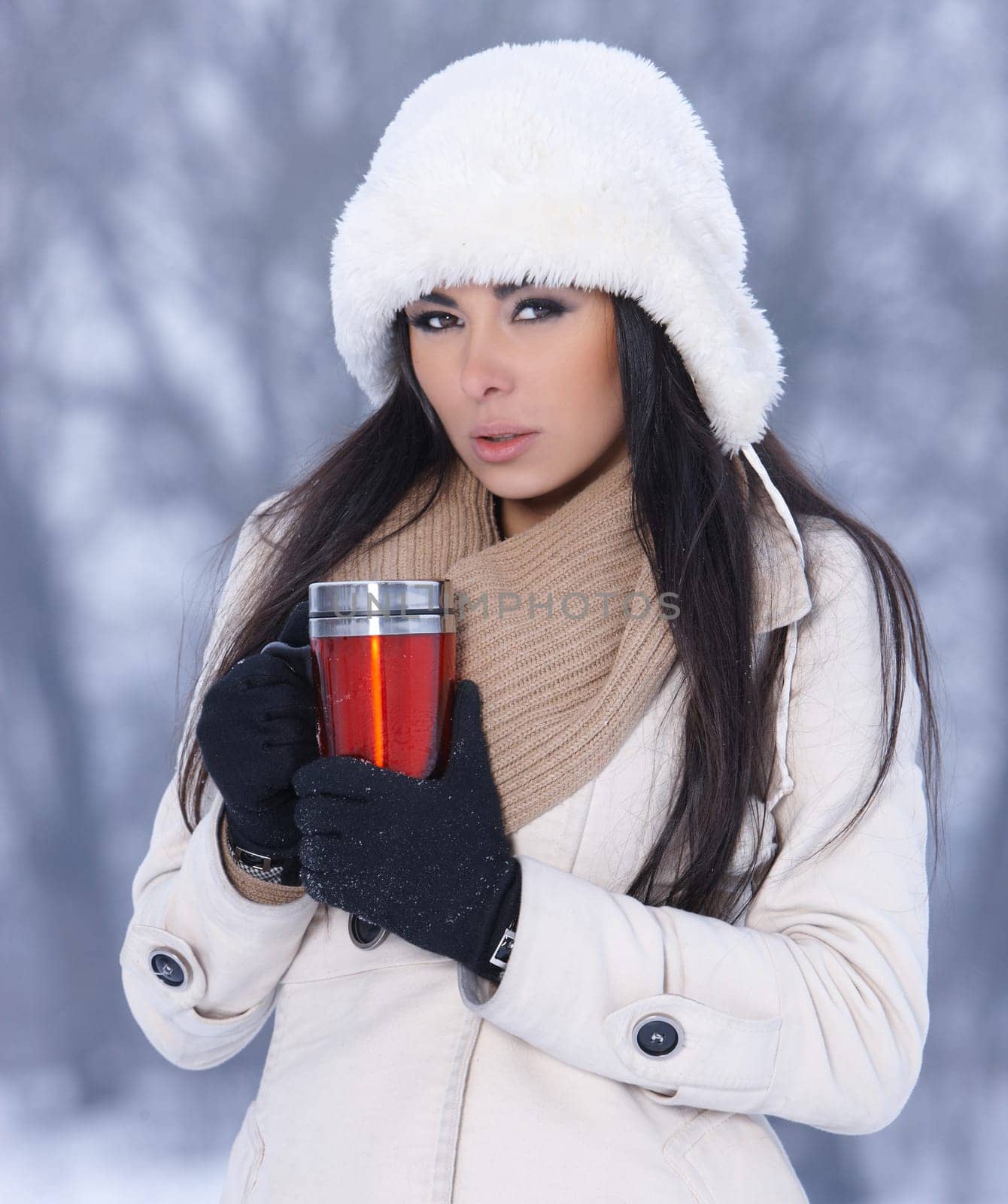 Beautiful woman holding thermal mug in snowy winter outdoors