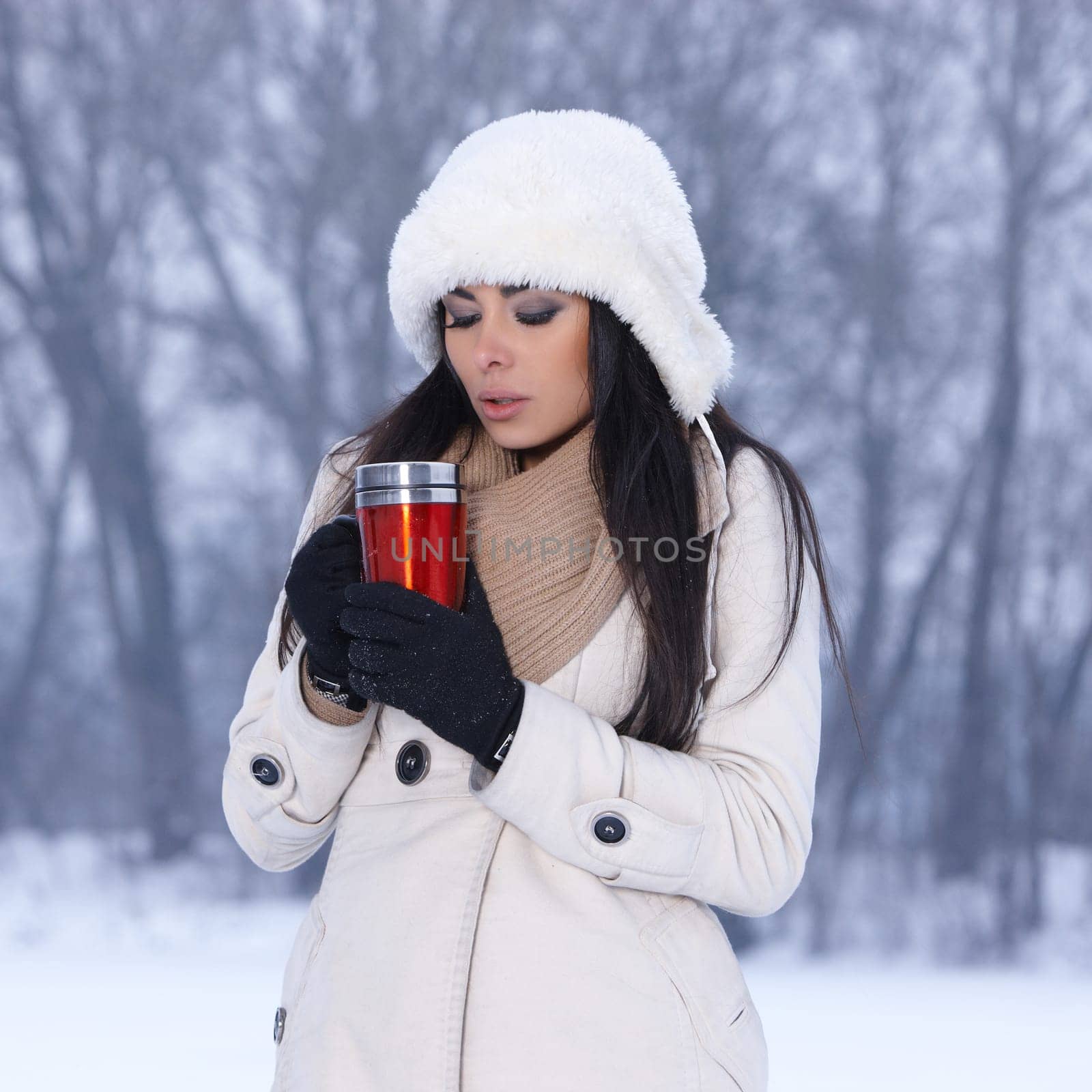 Beautiful woman holding thermal mug in snowy winter outdoors