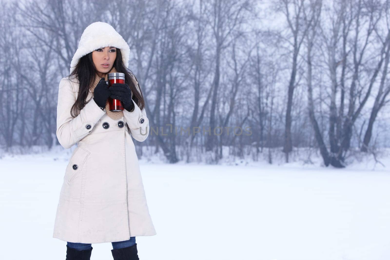 Beautiful woman holding thermal mug in snowy winter outdoors