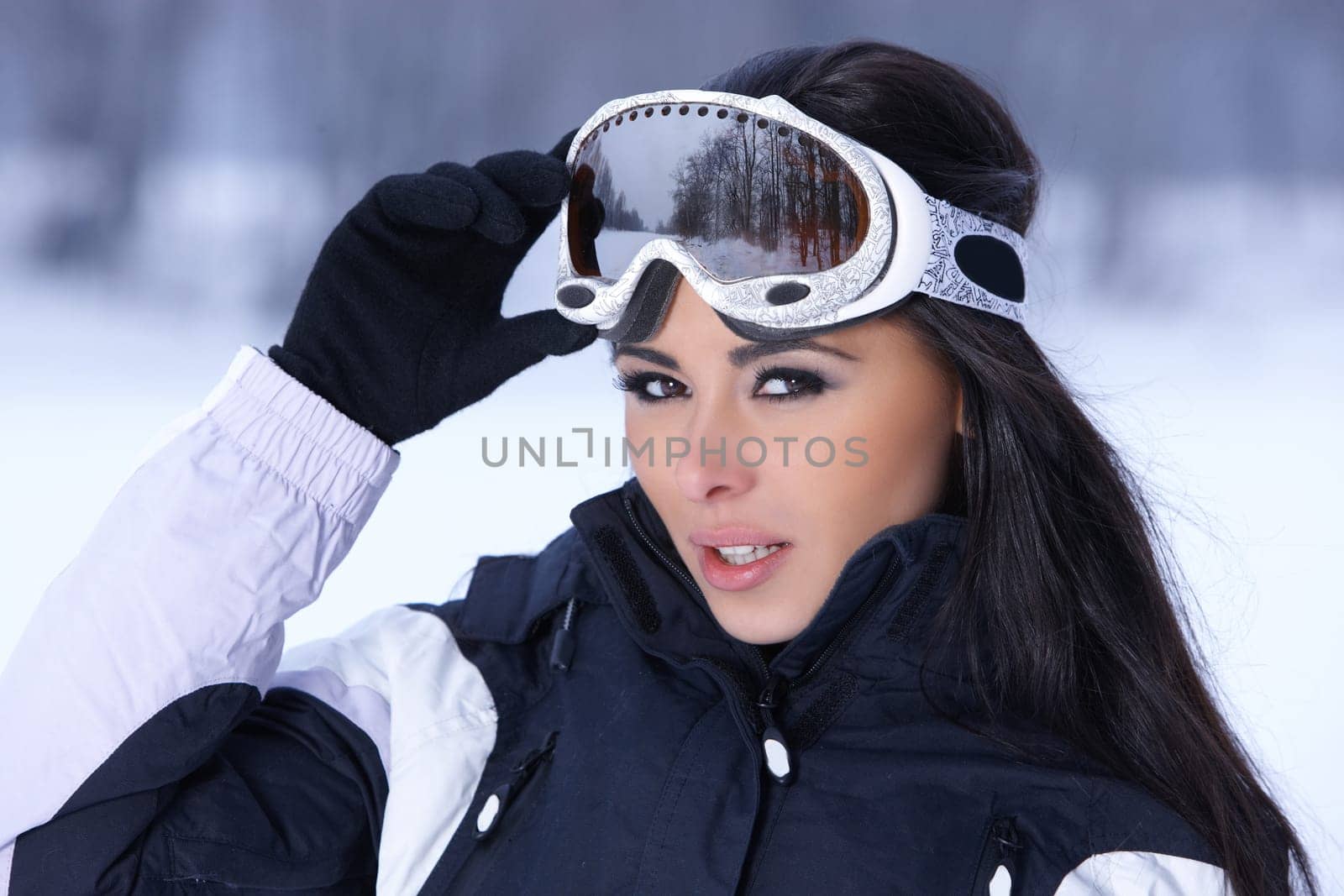 Beautiful woman wearing goggles in snowy winter outdoors